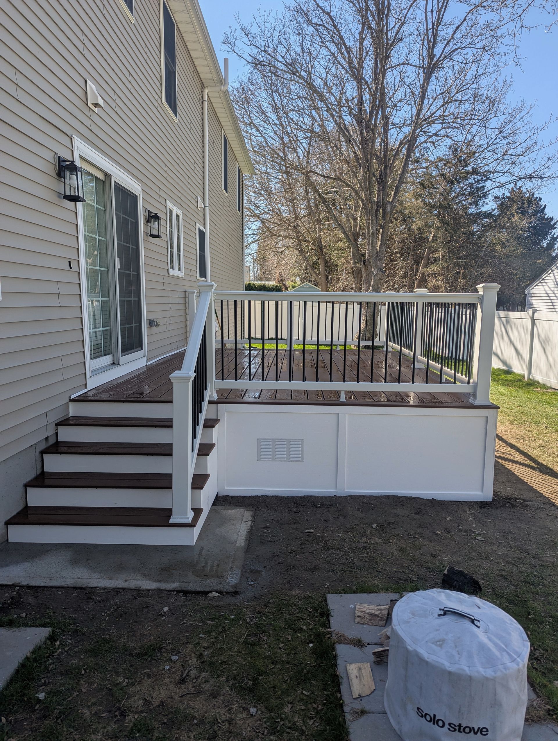 A tan house with a new composite deck featuring white railings, dark brown steps and flooring, and white lattice skirting. 
