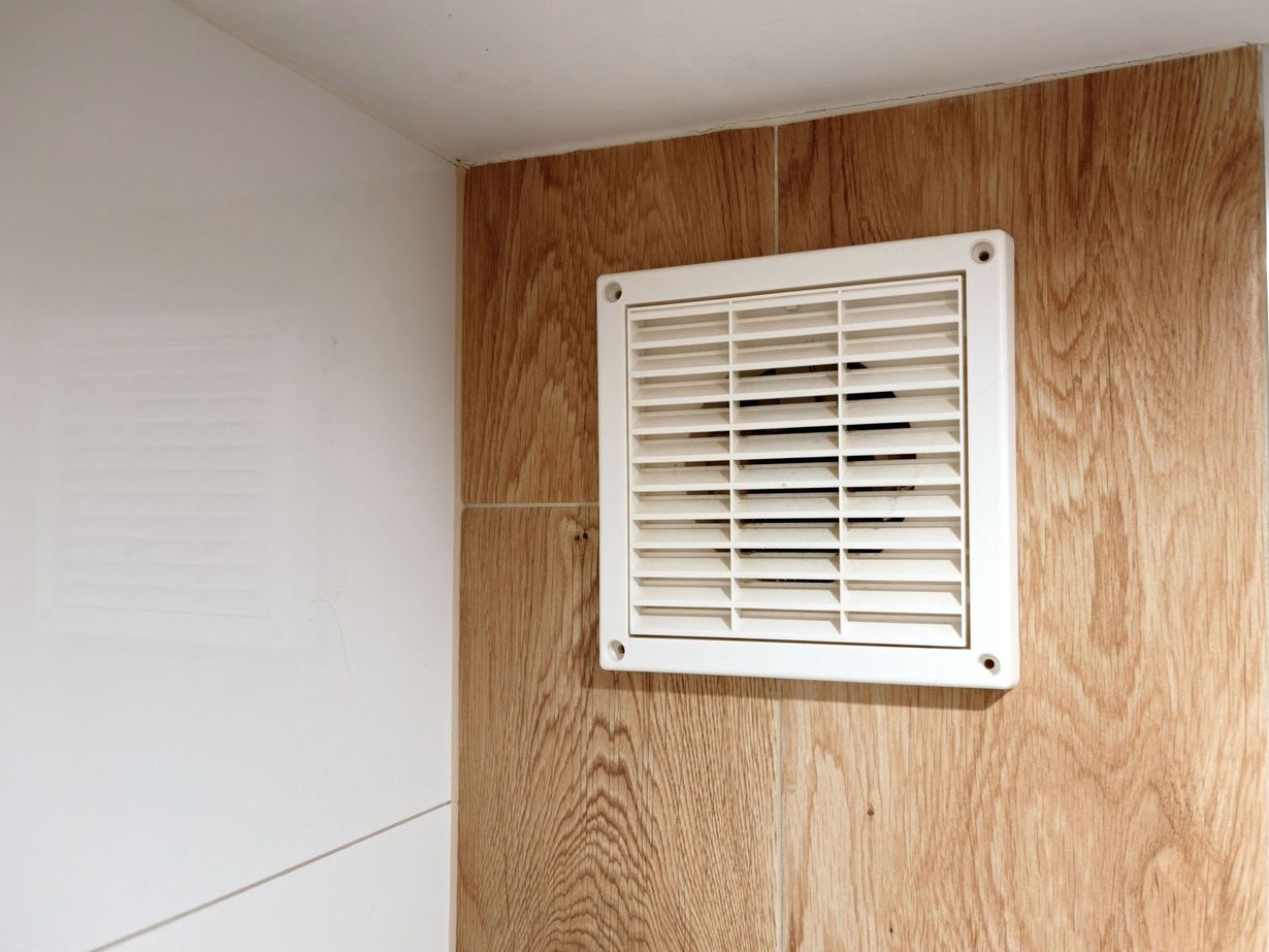 White wall vent on a wood-paneled corner wall.