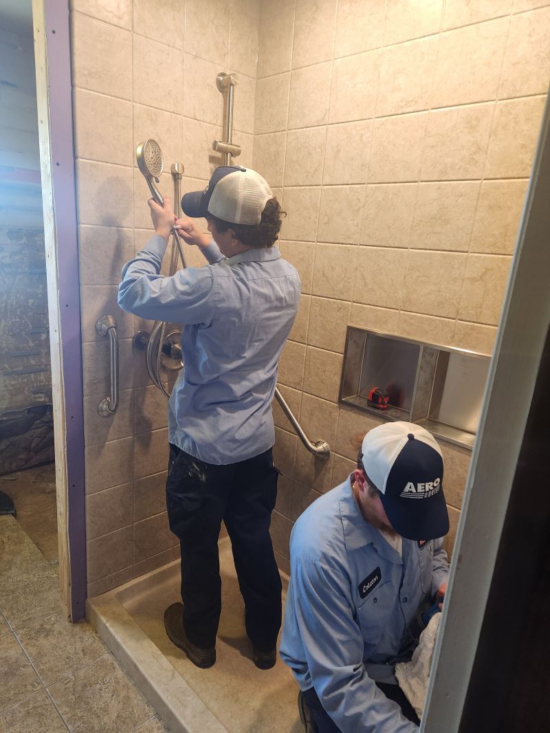 Two workers installing shower hardware in a tiled bathroom stall