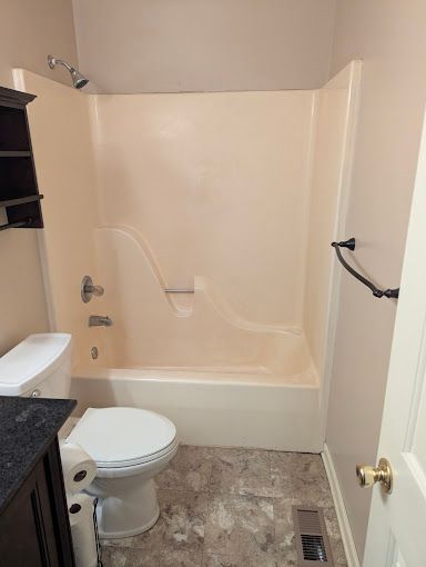 Small bathroom with beige tub-shower, white toilet, granite vanity, and towel rack.