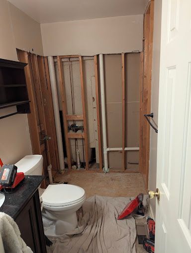 Bathroom under renovation with exposed wall studs, toilet, and construction tools.