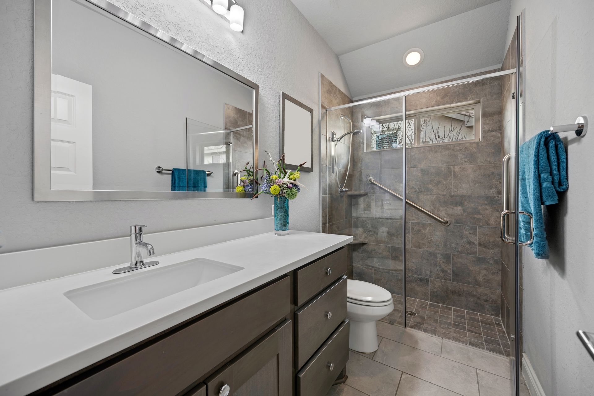 Modern bathroom with double vanity, large mirror, and glass walk-in shower; teal towels hang on the wall