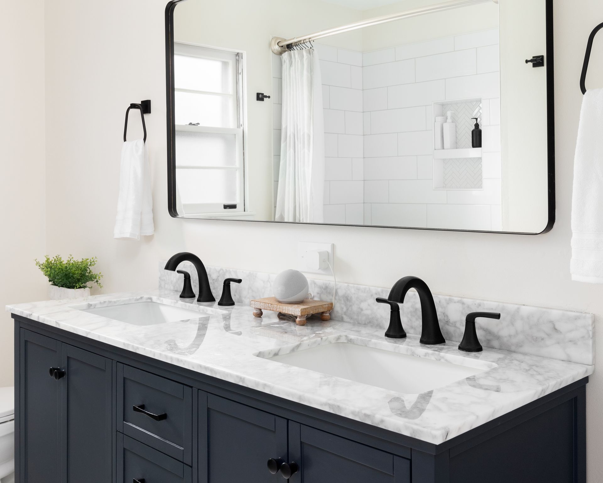 Modern bathroom vanity with black cabinets, white marble countertop, and large mirror