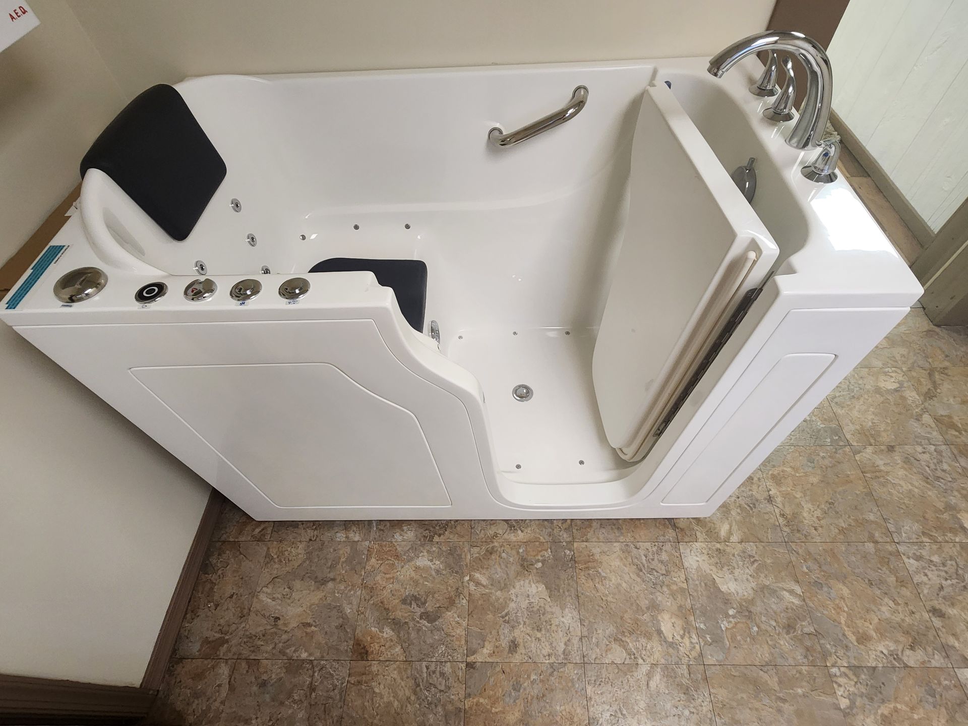 White walk-in bathtub with open door, built-in seat, grab bars, and control buttons in a bathroom.