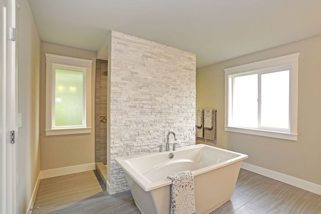 Bright bathroom with freestanding tub, walk-in shower, and two windows in neutral tones