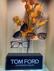 Tom Ford display with eyeglasses on a stand and orange decorative leaves behind it