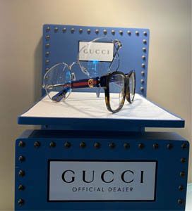 Gucci eyeglasses displayed on a blue and white Gucci official dealer stand.