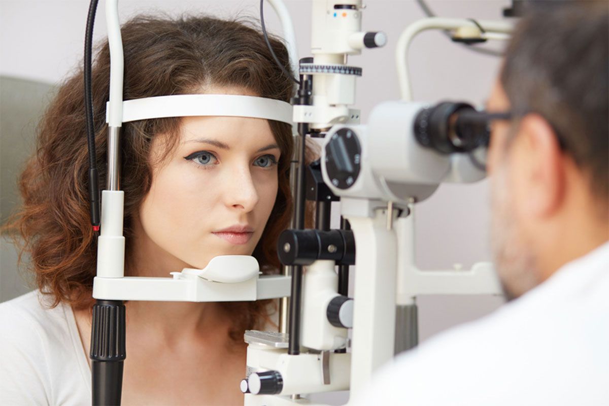 Woman at an eye exam looking into a slit lamp while an optometrist examines her eye