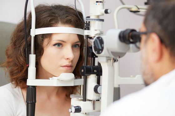 Woman at an eye exam looking into a slit lamp while an optometrist examines her eye