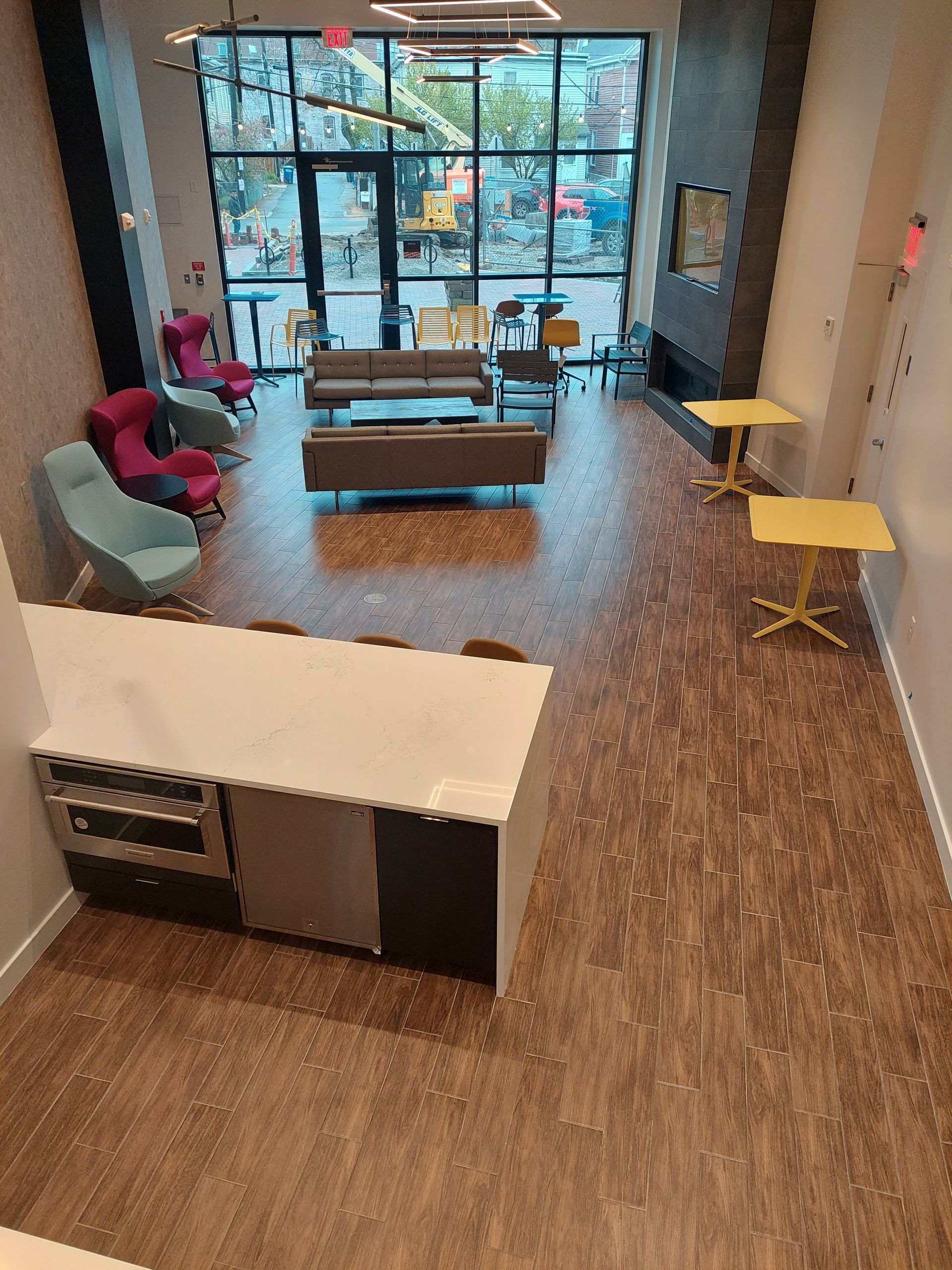 Spacious modern lounge with seating, kitchen island, large windows, and yellow tables.