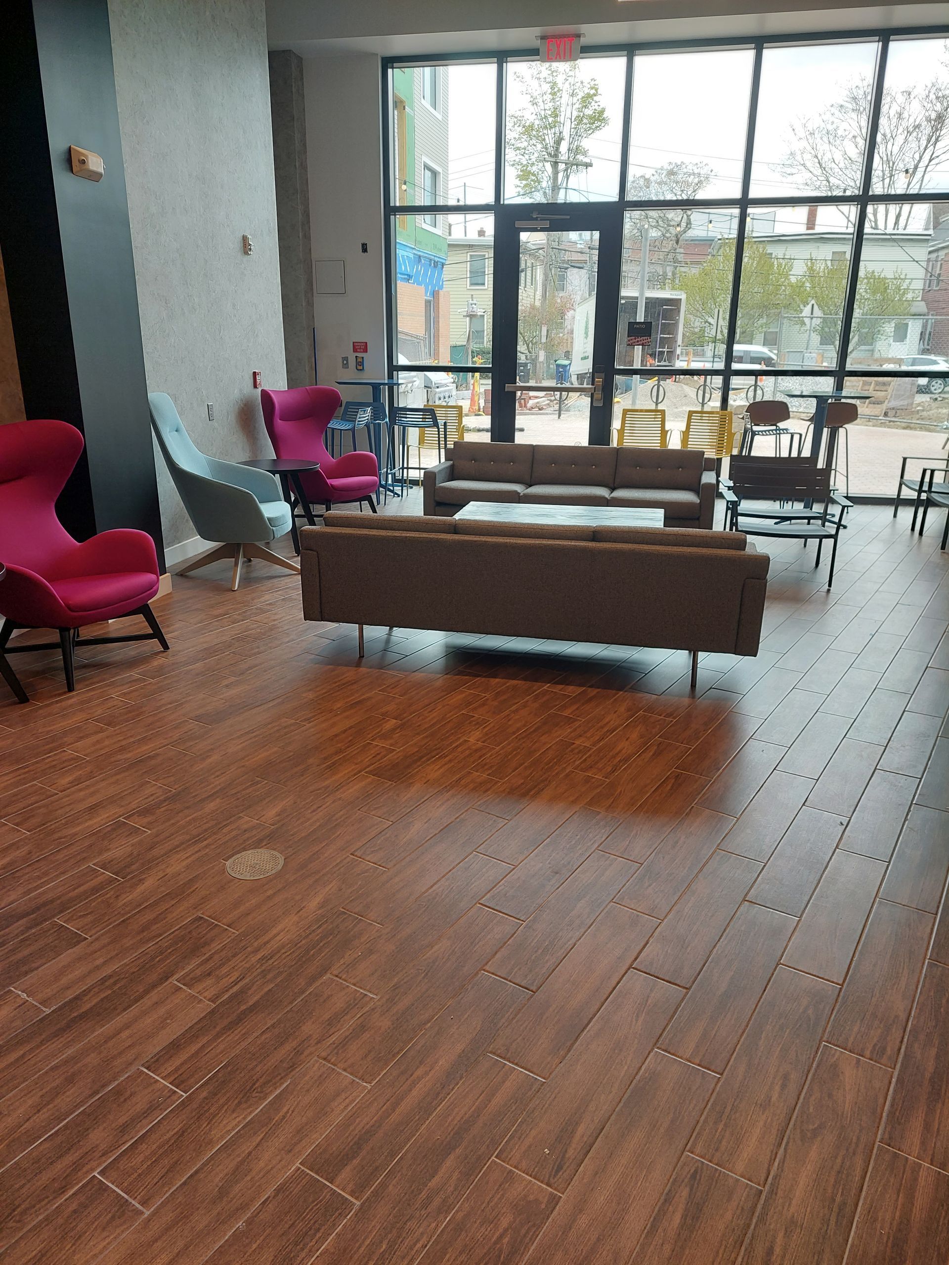 Lounge area with colorful chairs, brown couches, and large windows looking onto a street.