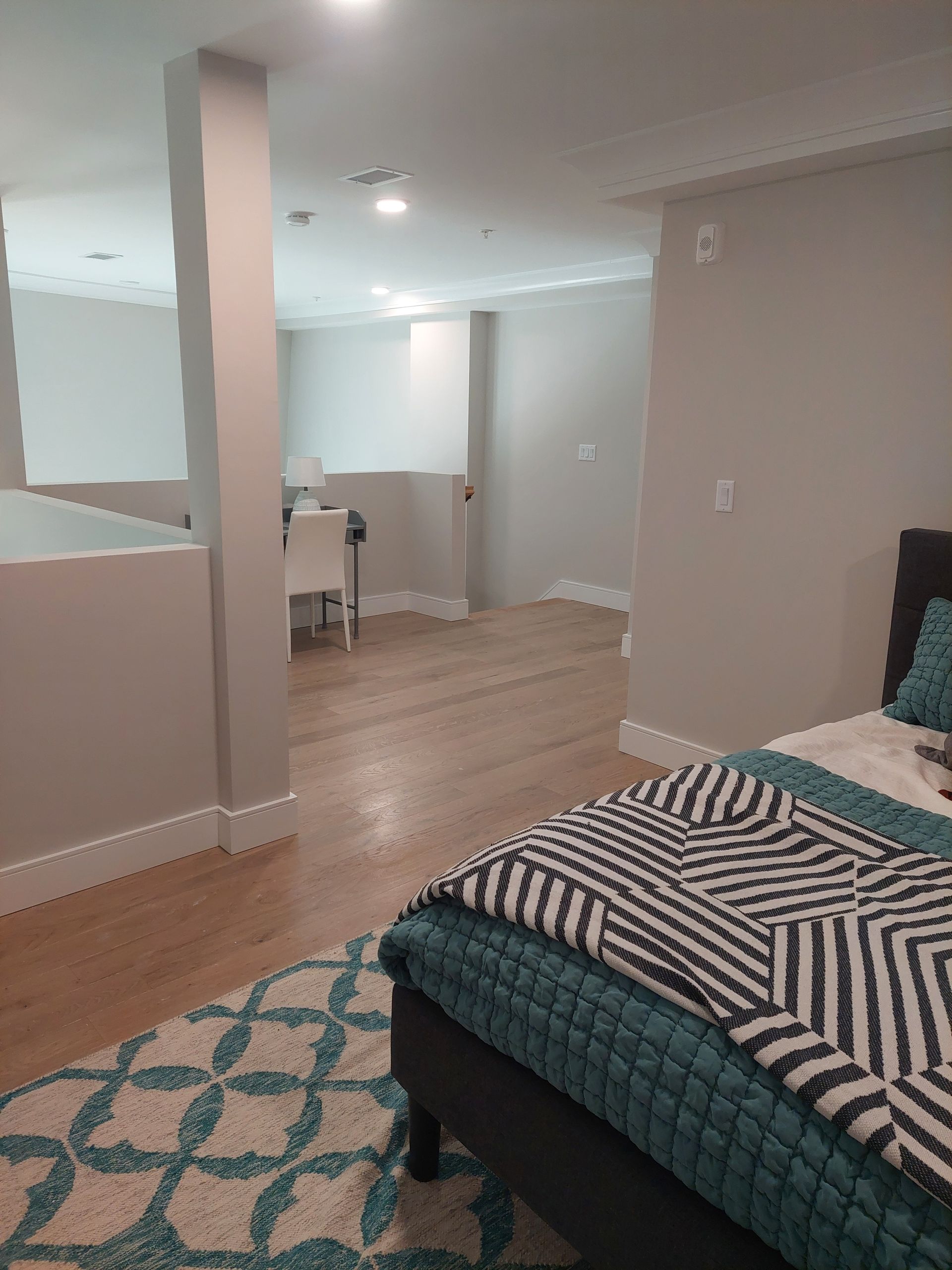 Bedroom with hardwood floors and teal rug; bed with striped throw blanket; view into hallway.