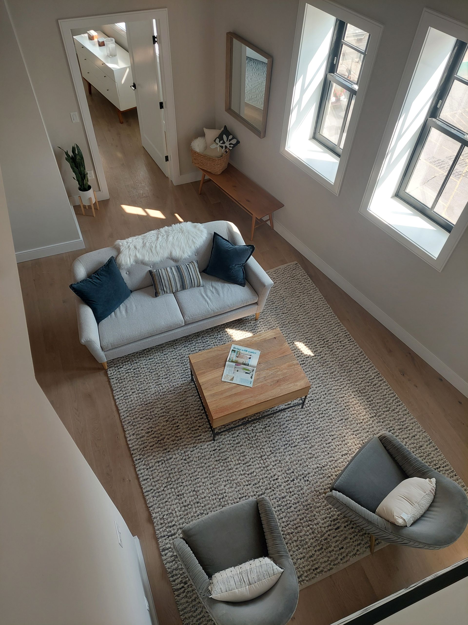 High-angle view of a modern living room: a gray sofa, two armchairs, a rug, and a wooden coffee table.