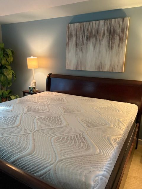 Bedroom with a dark wood bed, white quilt, blue walls, lamp, plant, and abstract wall art