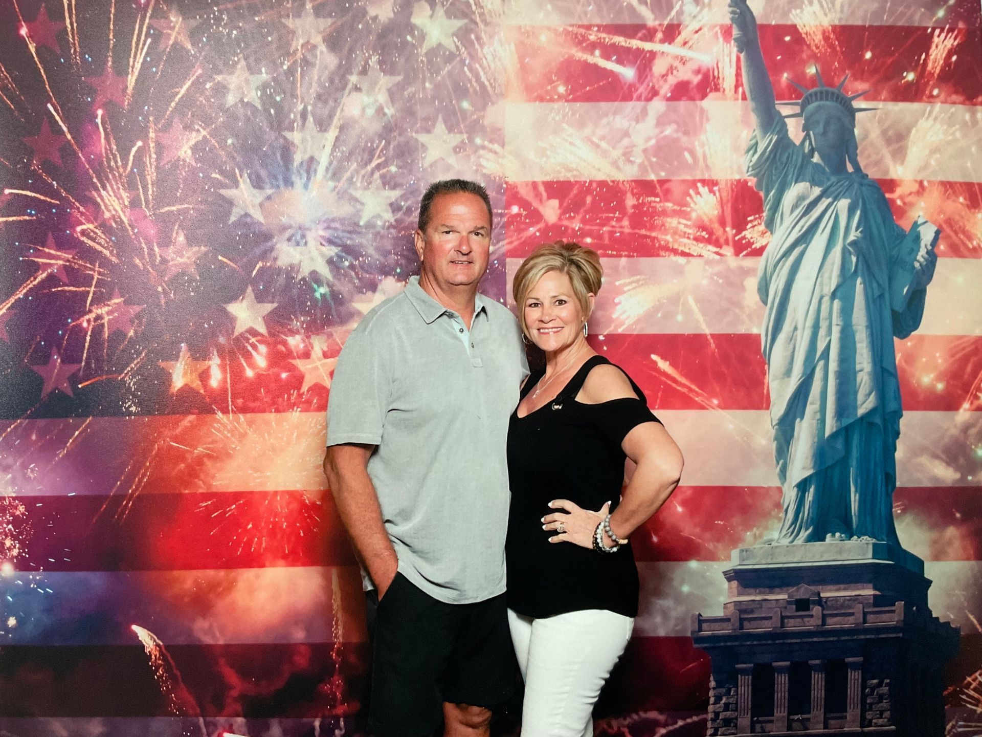 A man and woman are posing for a picture in front of an american flag and statue of liberty