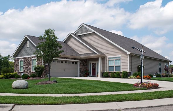 Suburban home with beige siding, brick accents, and a curved driveway on a sunny day.