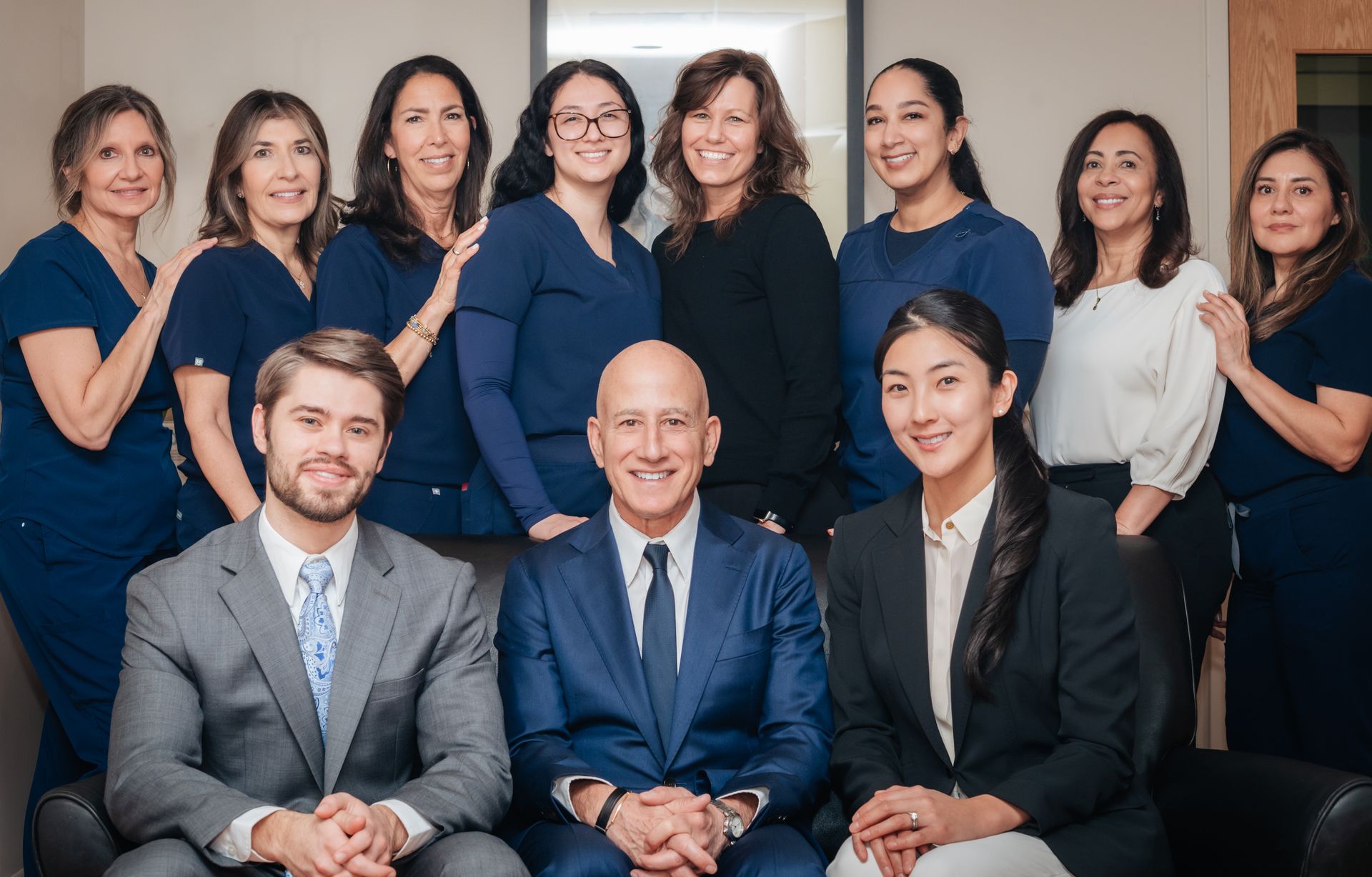 A group of 11 medical and office professionals standing and sitting together for a formal portrait in an office setting.