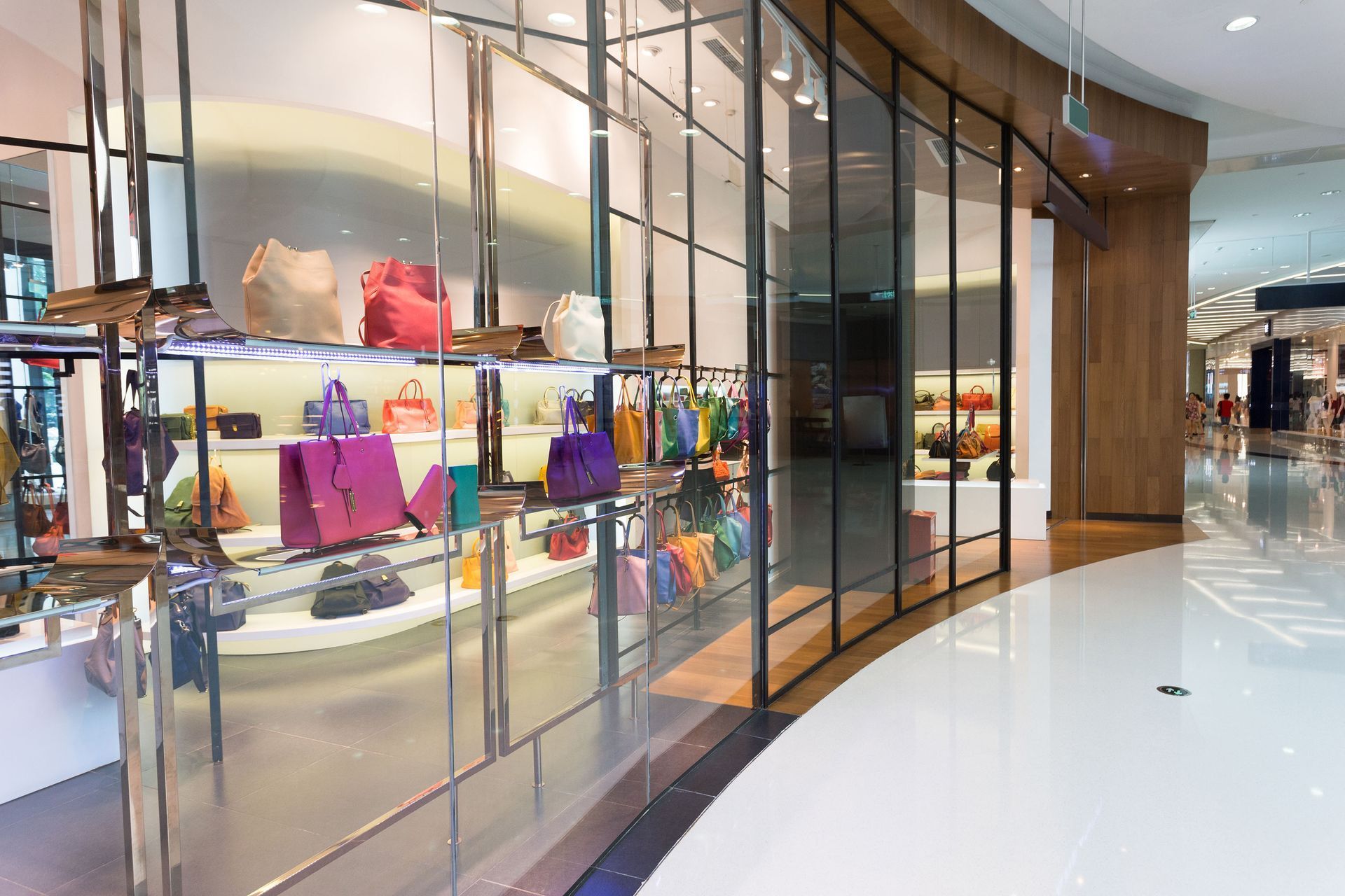 Handbag display in a brightly lit retail store with curved glass windows and polished floors.