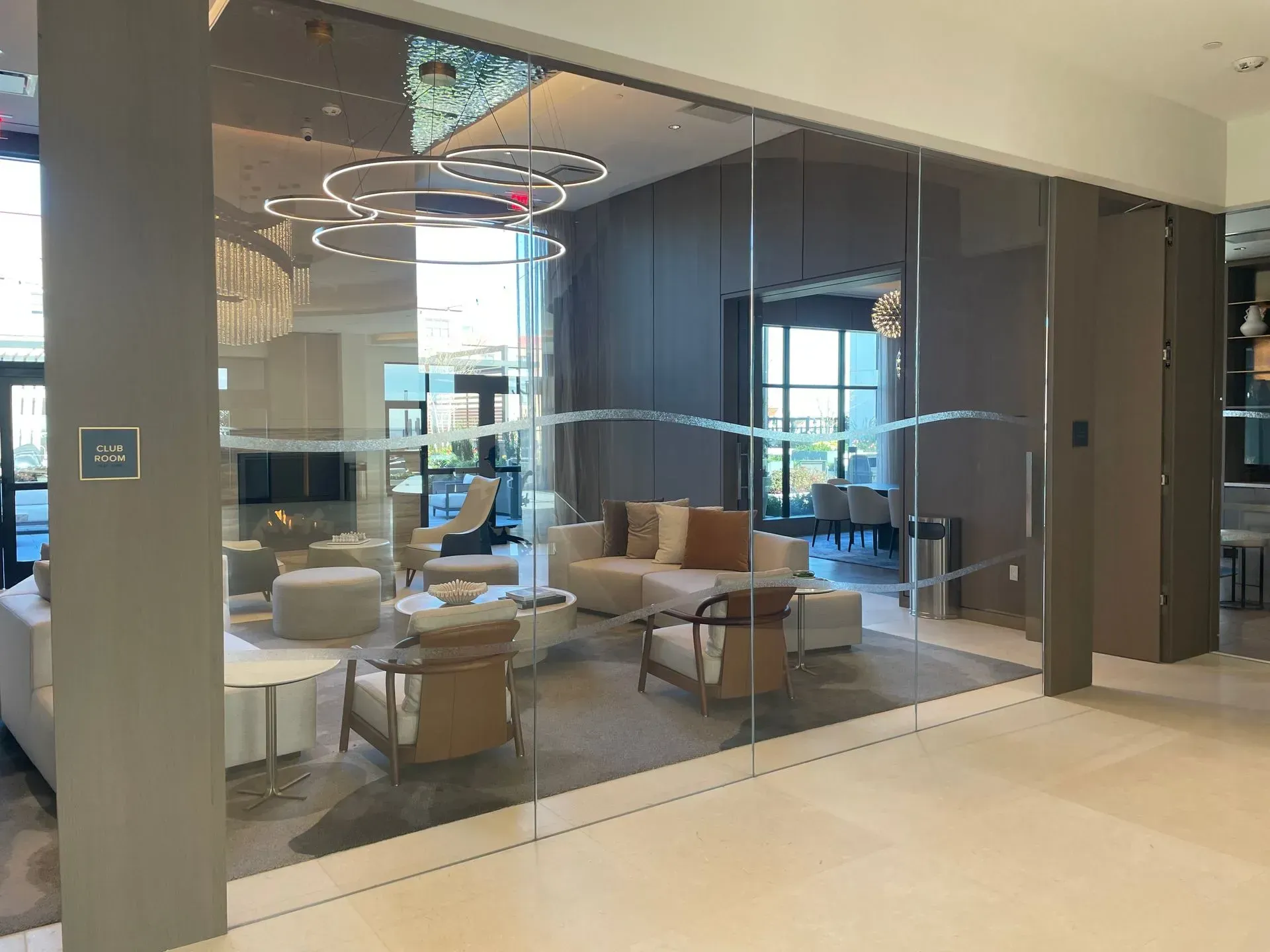 Modern waiting area with glass walls, couches, chairs, and decorative lighting.