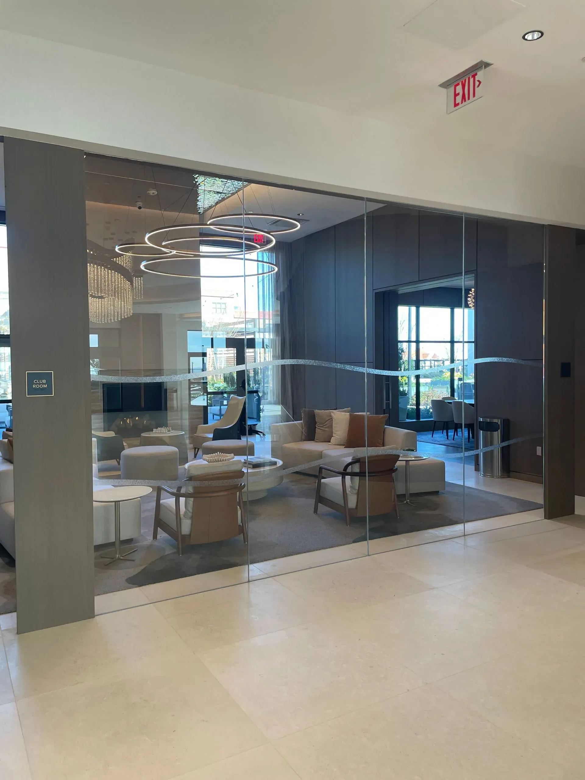 Modern lounge with glass walls, cream-colored sofas and chairs, and a bright, airy setting.