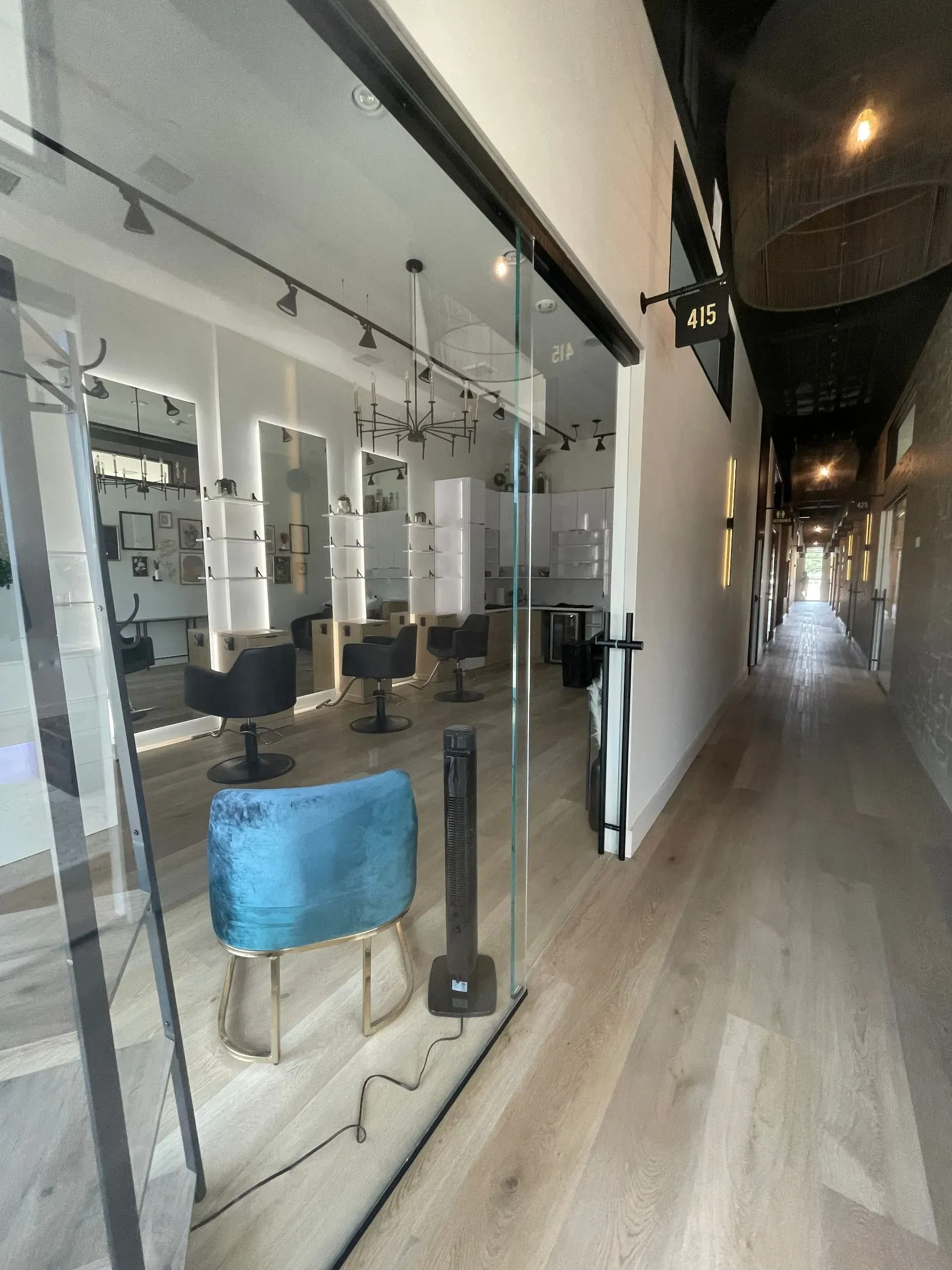 Hair salon interior with glass storefront, chairs, mirrors, and a hallway.