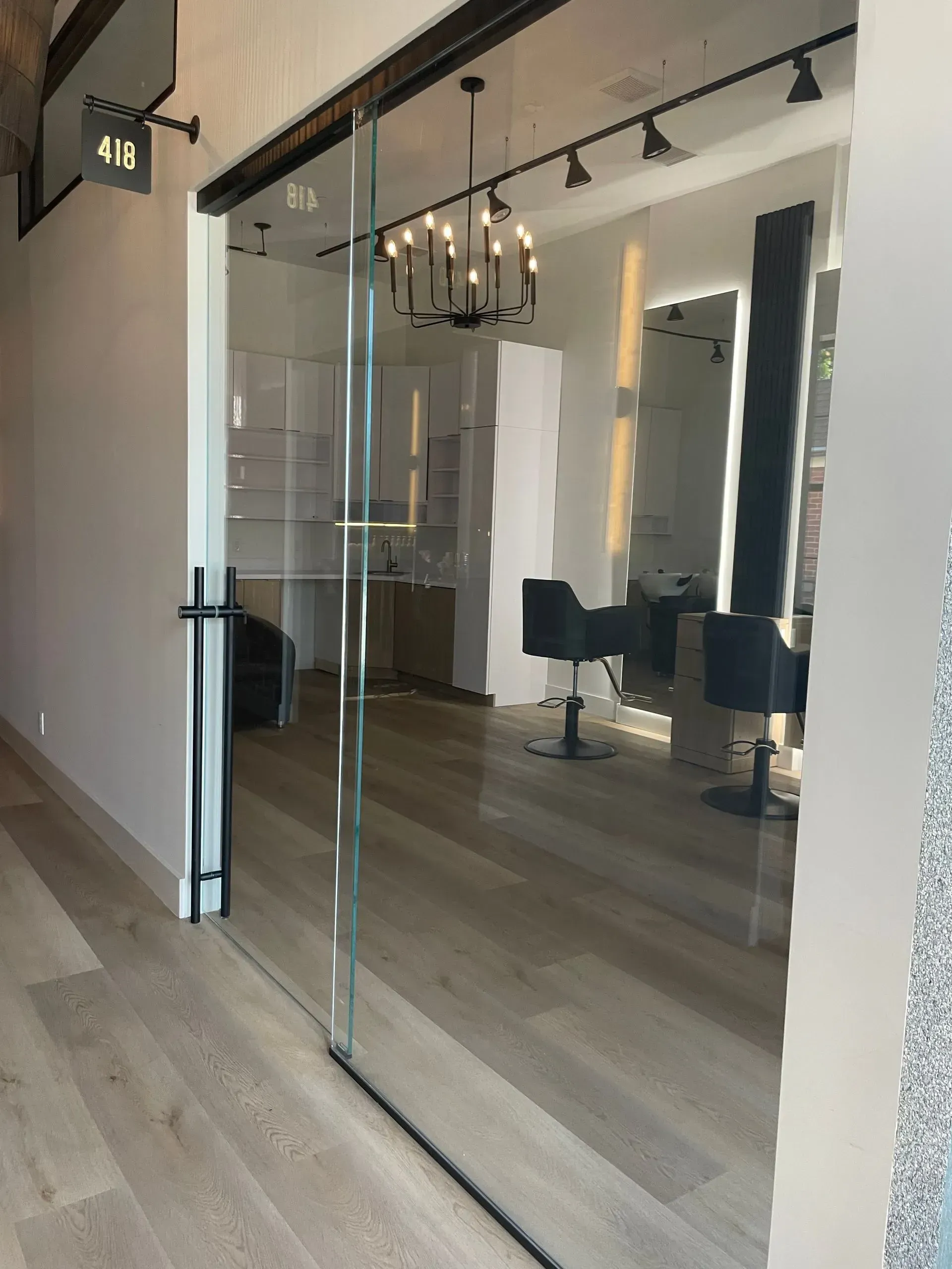 Glass sliding door to a hair salon with chairs, mirrors, and a chandelier; wooden floors.