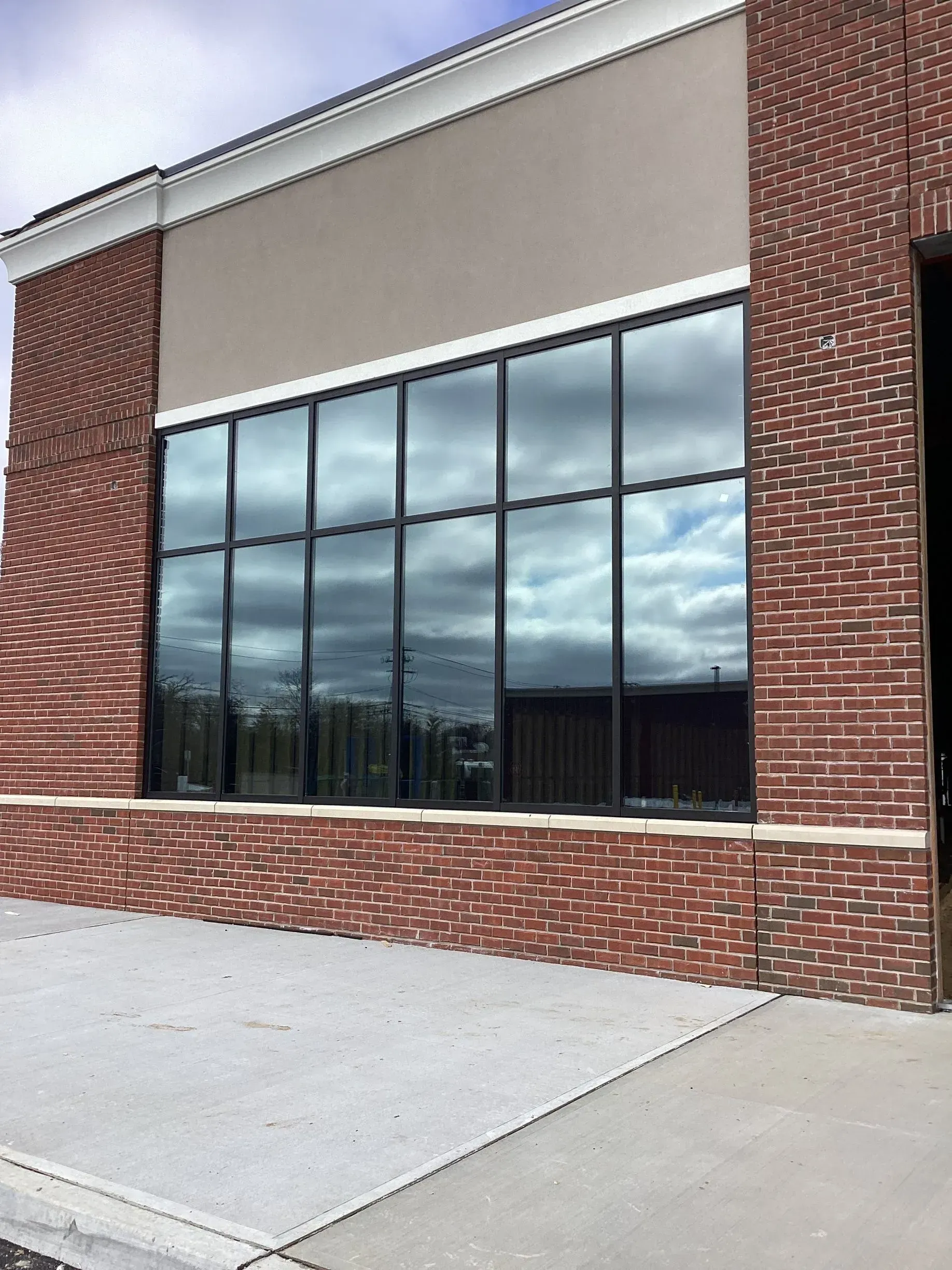 Building exterior with large windows reflecting sky. Red brick and beige facade with a concrete sidewalk.