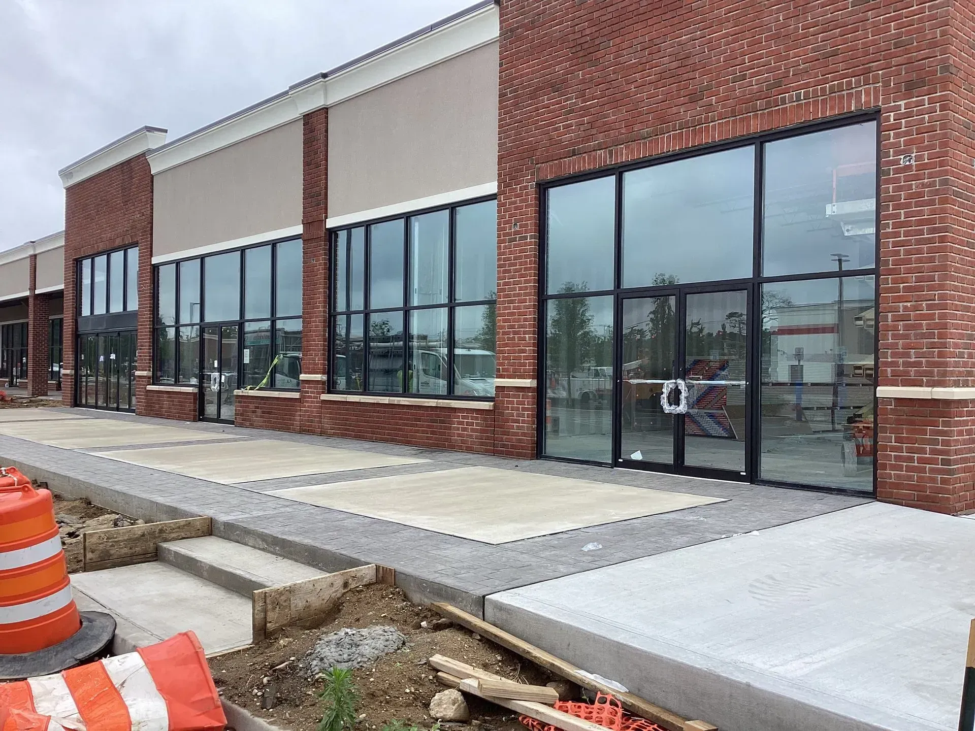 Exterior of a brick commercial building with large windows; sidewalk under construction with orange cones.