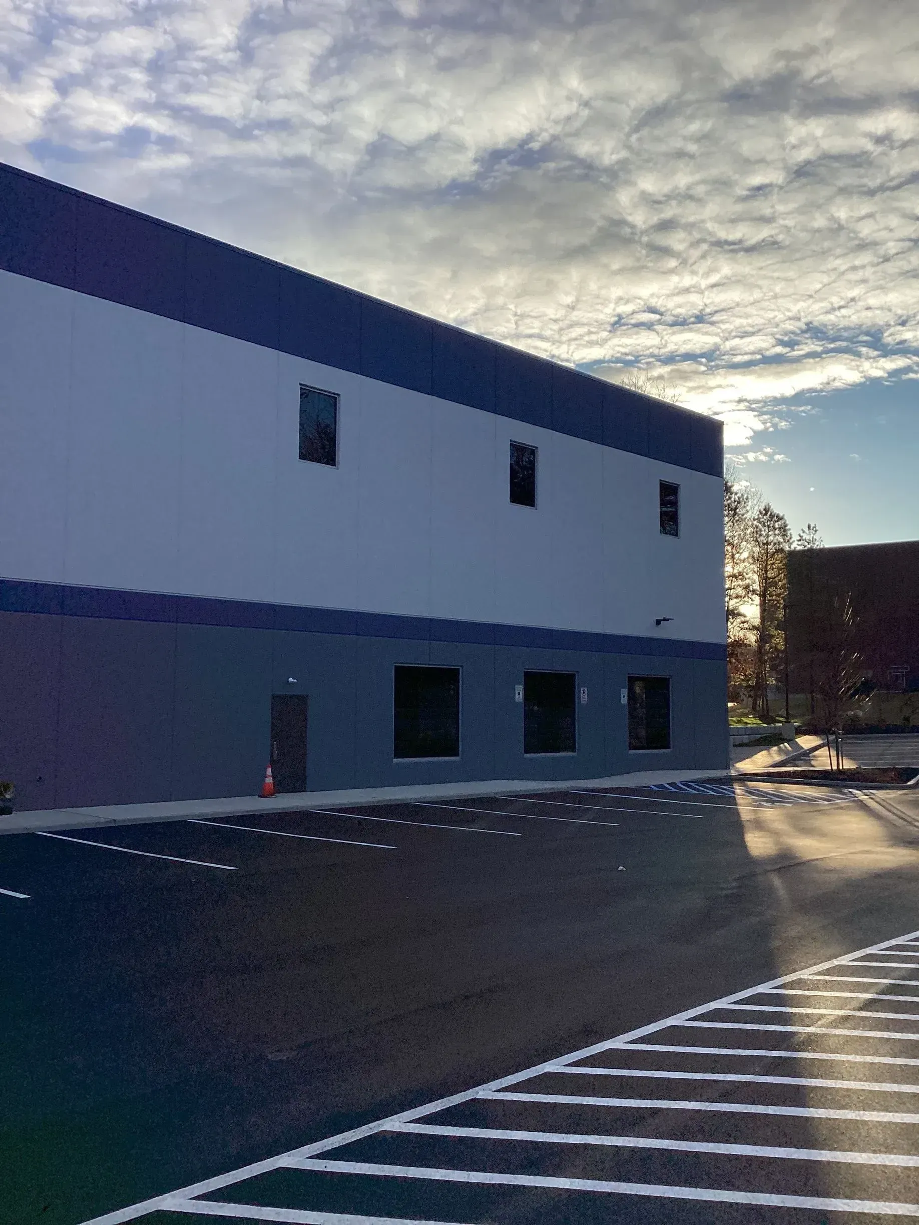 Large commercial building with gray and blue exterior, small windows, and asphalt parking lot.