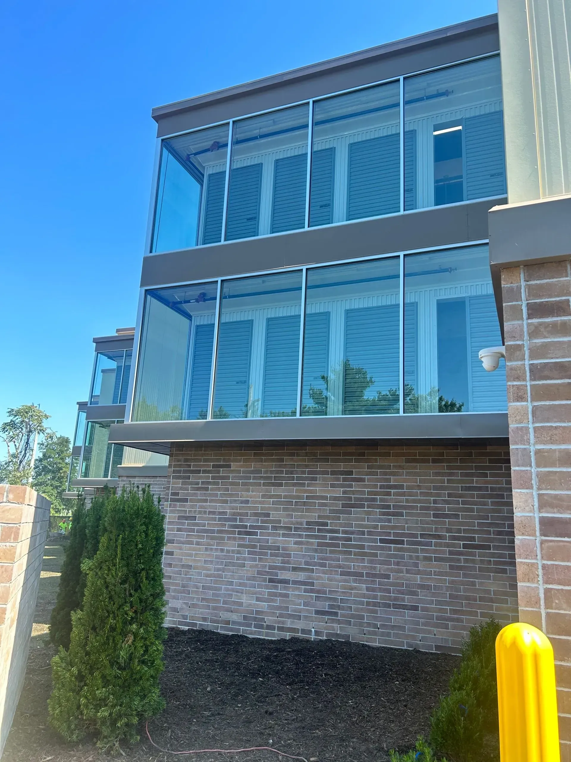 Two-story building with glass balconies, atop a brick wall, against a blue sky.