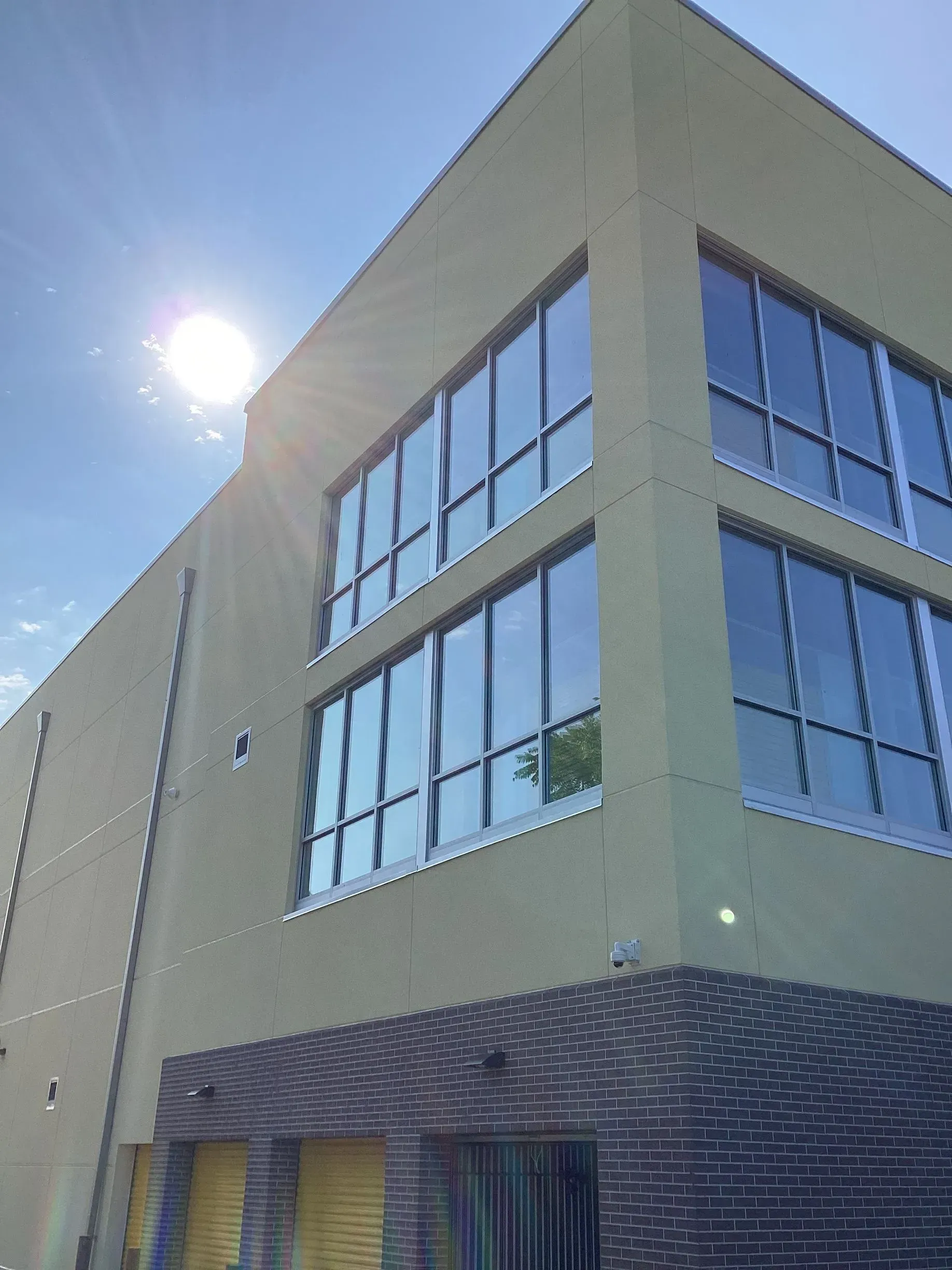 Building with large windows, tan stucco exterior, brick base. Sunny sky in background.