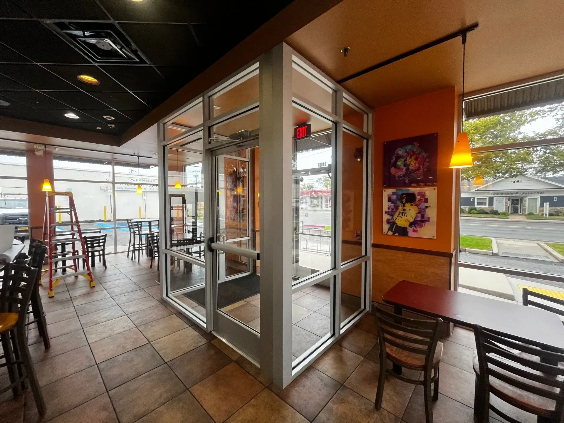 Interior of a restaurant with glass walls, tables, chairs, and art.