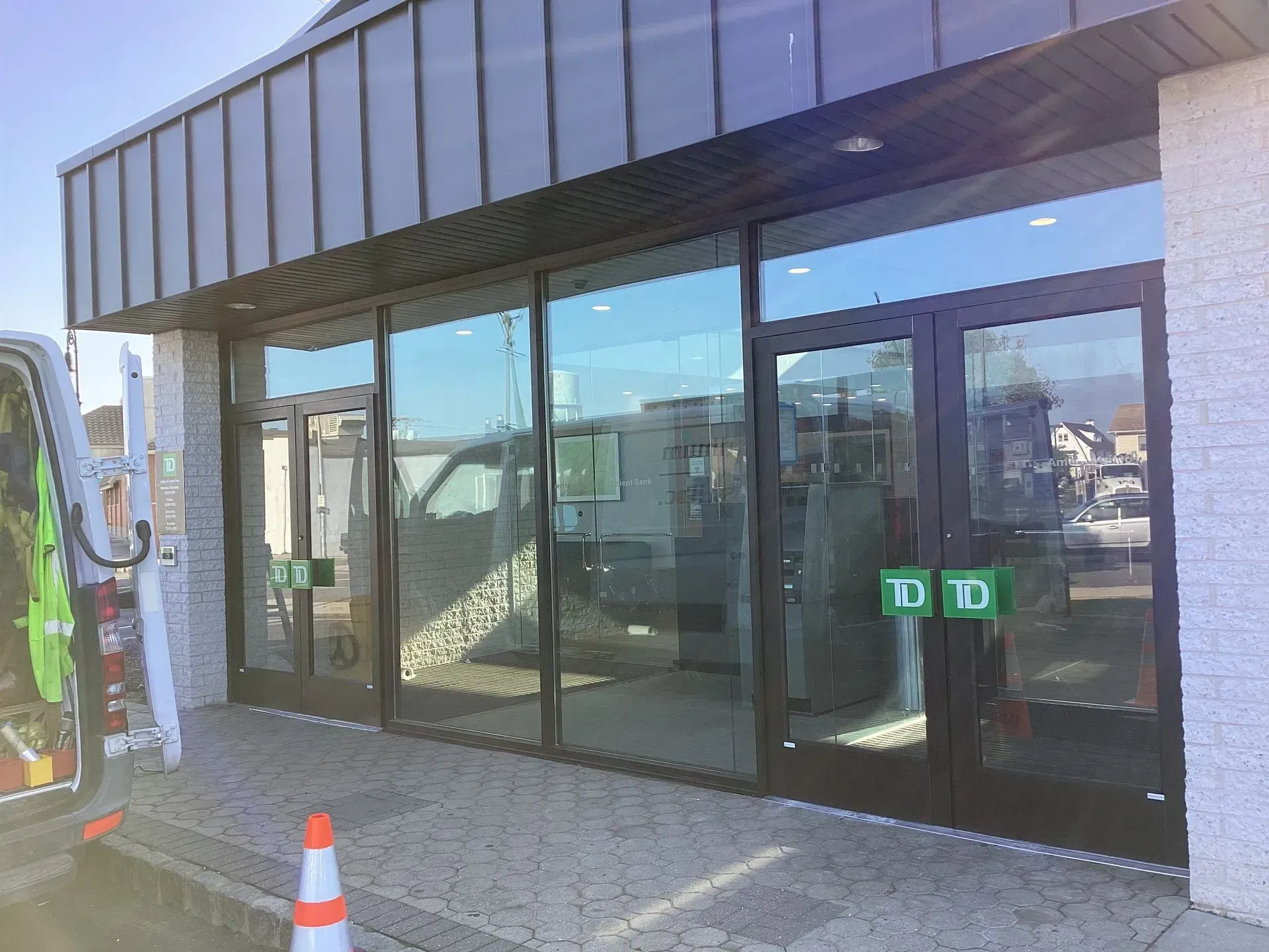Exterior of a TD bank with glass doors and windows, silver roof, gray brick, and two green pull handles.