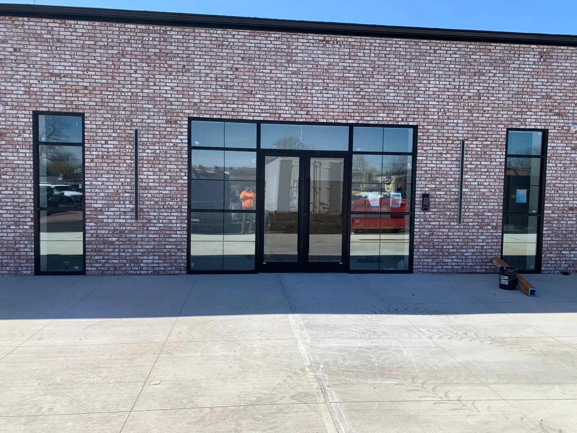 Brick building with black-framed windows and doors, set on a concrete slab; sunny day.