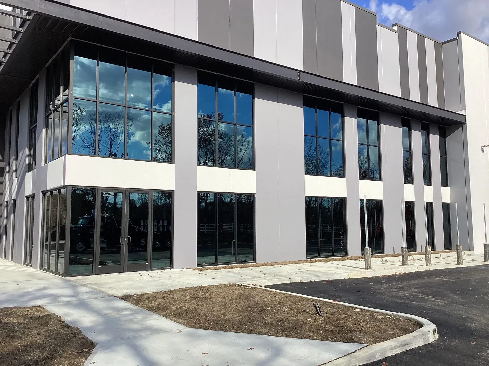 Modern building with large windows reflecting the sky and trees, gray and white exterior.