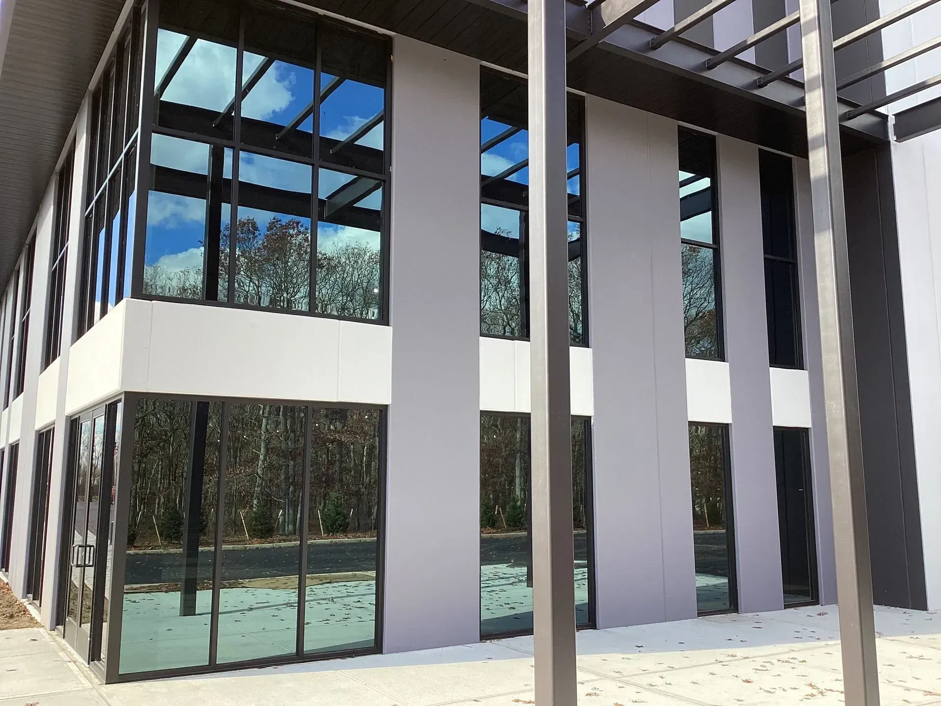 Exterior view of modern building with large glass windows reflecting a blue sky and surrounding trees.