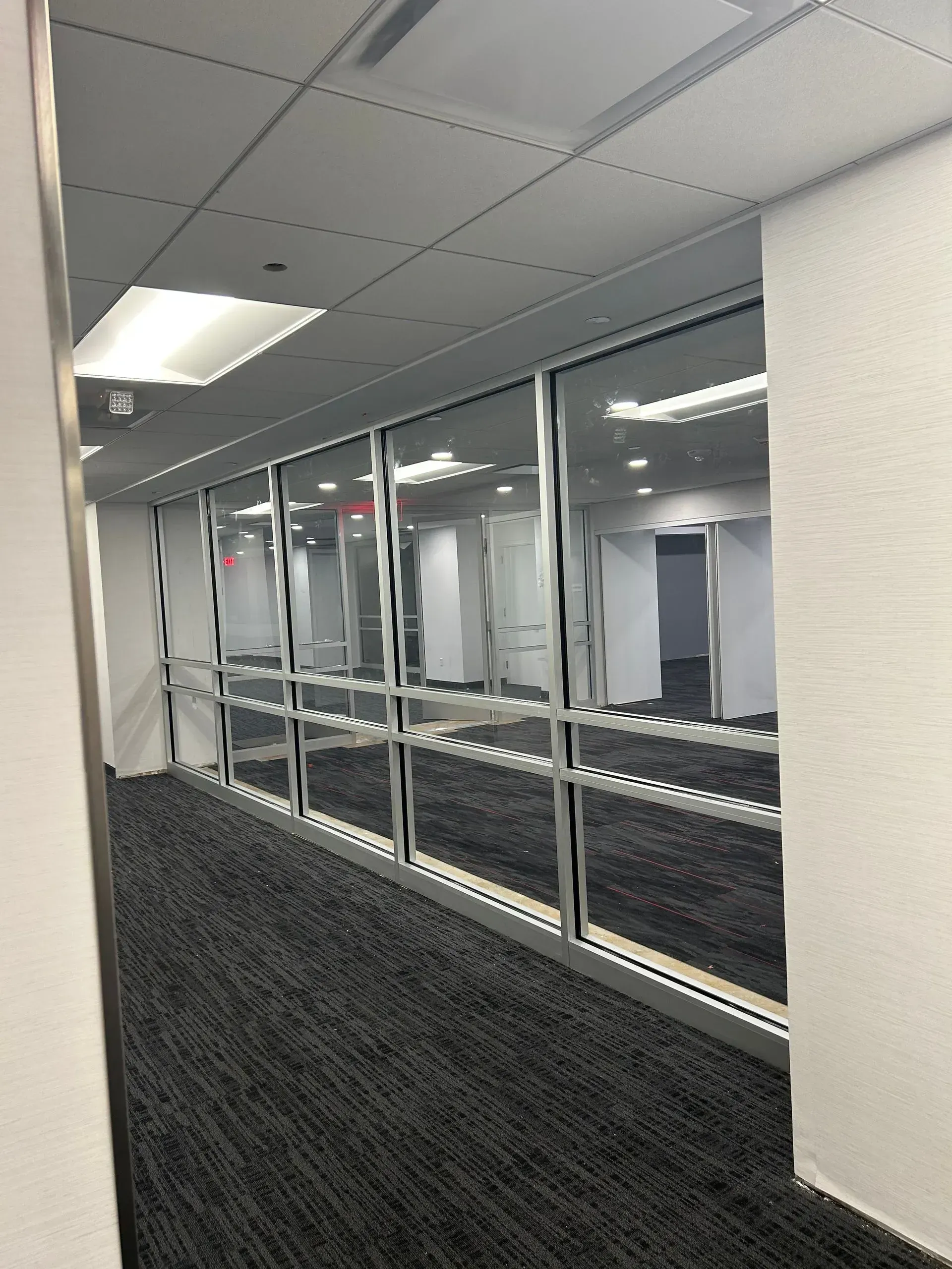 Office hallway with glass windows, carpet, and ceiling lights.