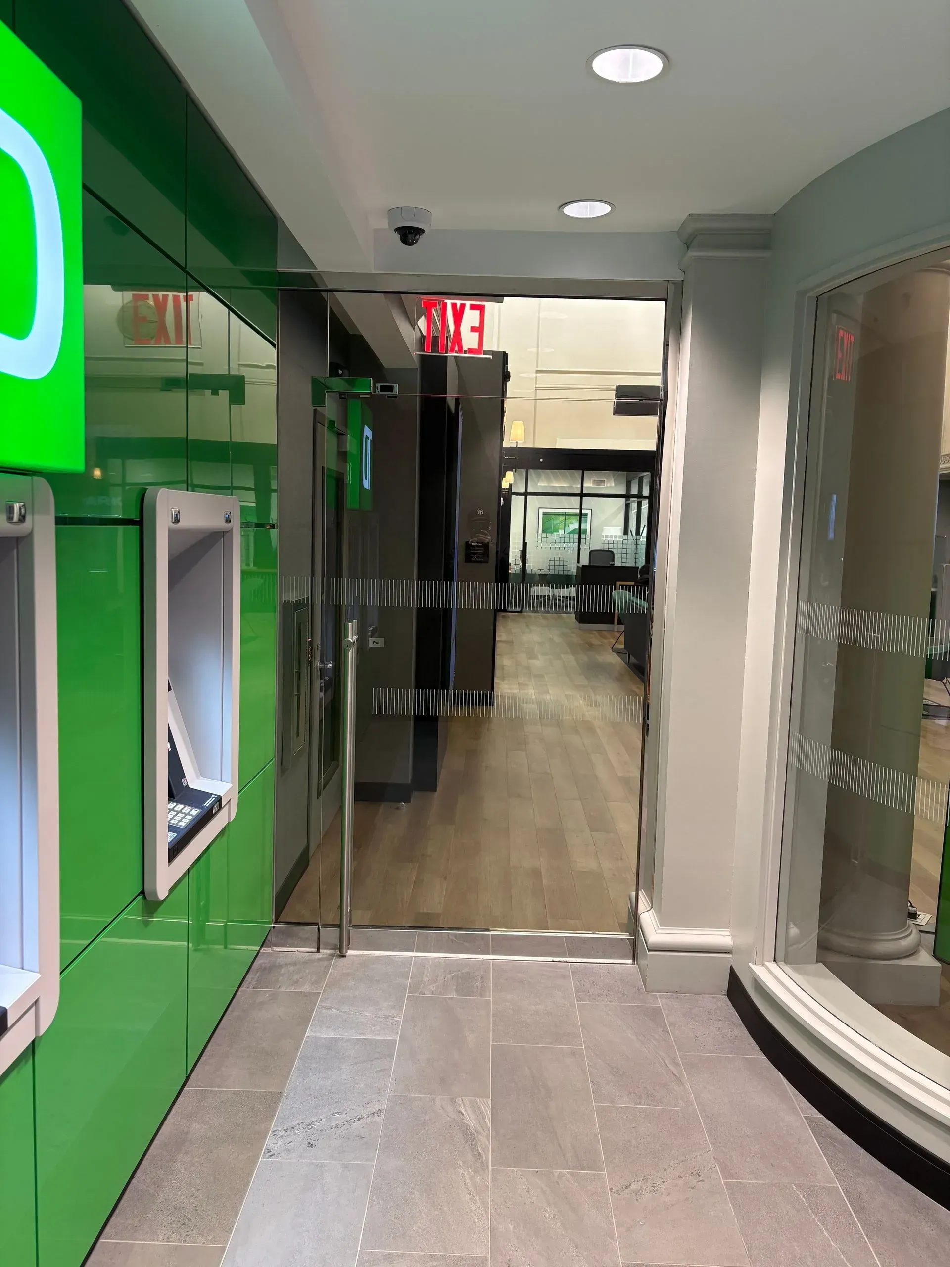 Interior of a bank with green and white accents, ATMs, and a glass door leading to the building's interior.
