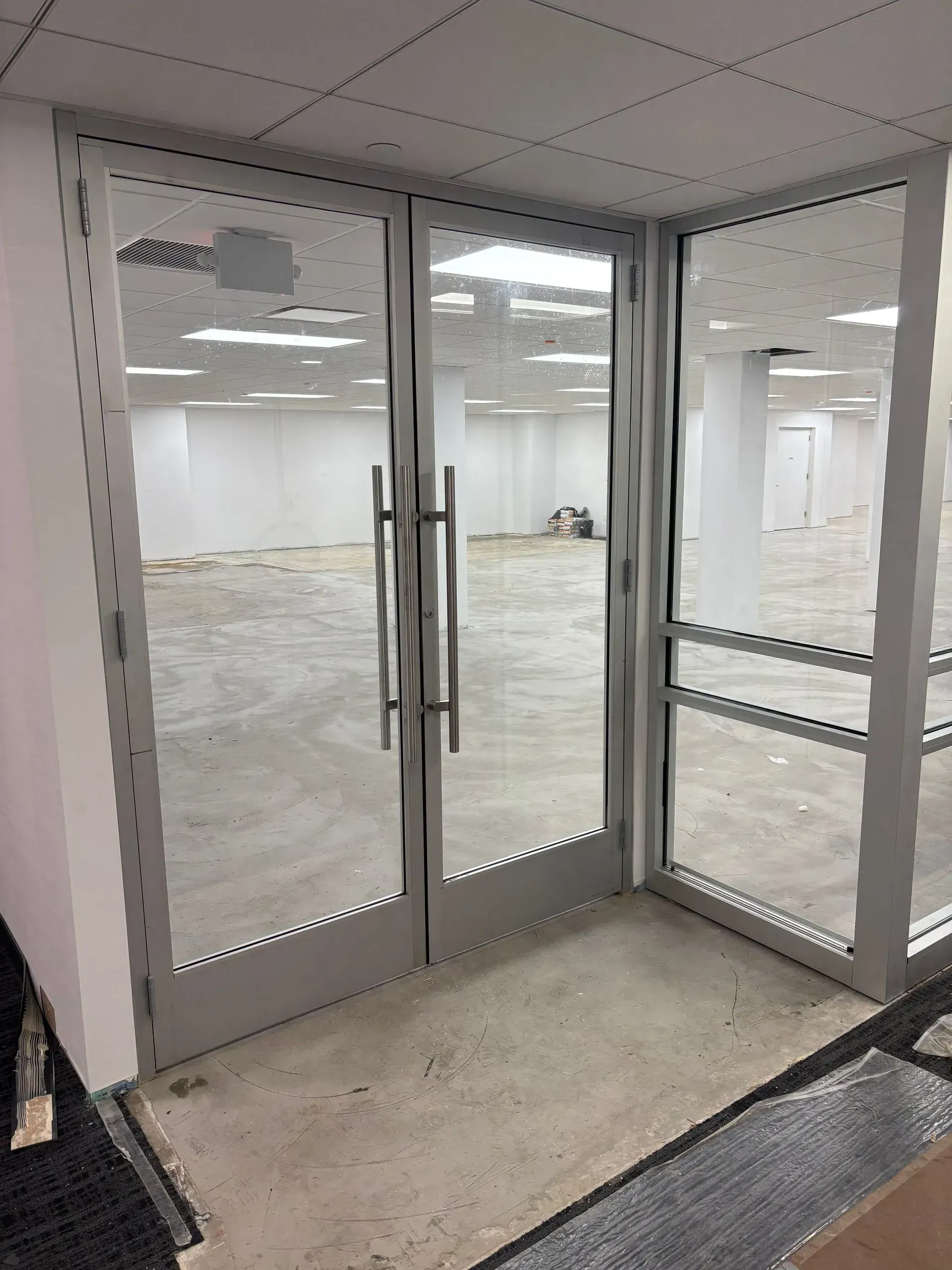 Glass double doors leading into an empty room with a concrete floor, surrounded by white walls.