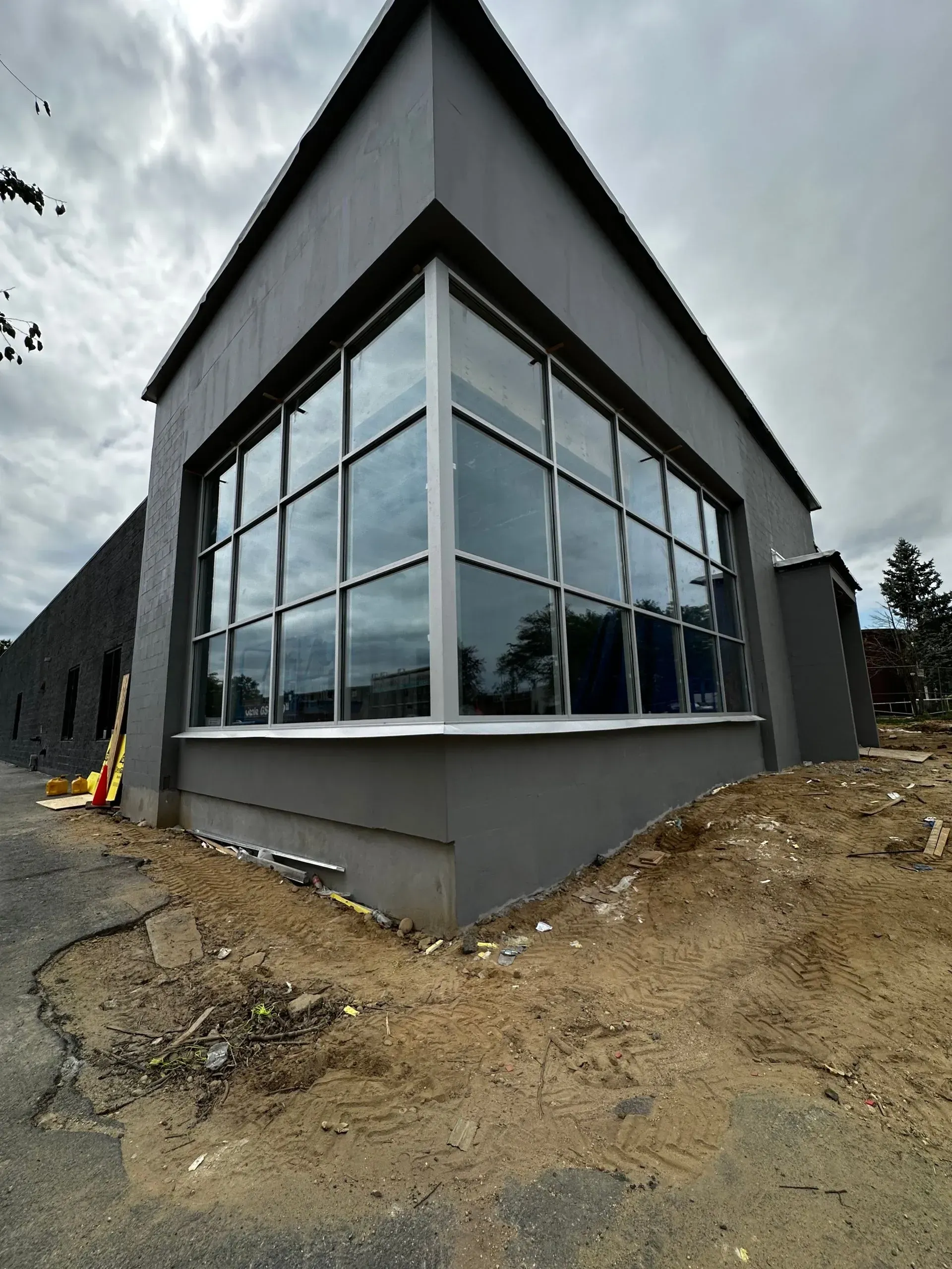 Gray building with large corner windows, cloudy sky, construction site.