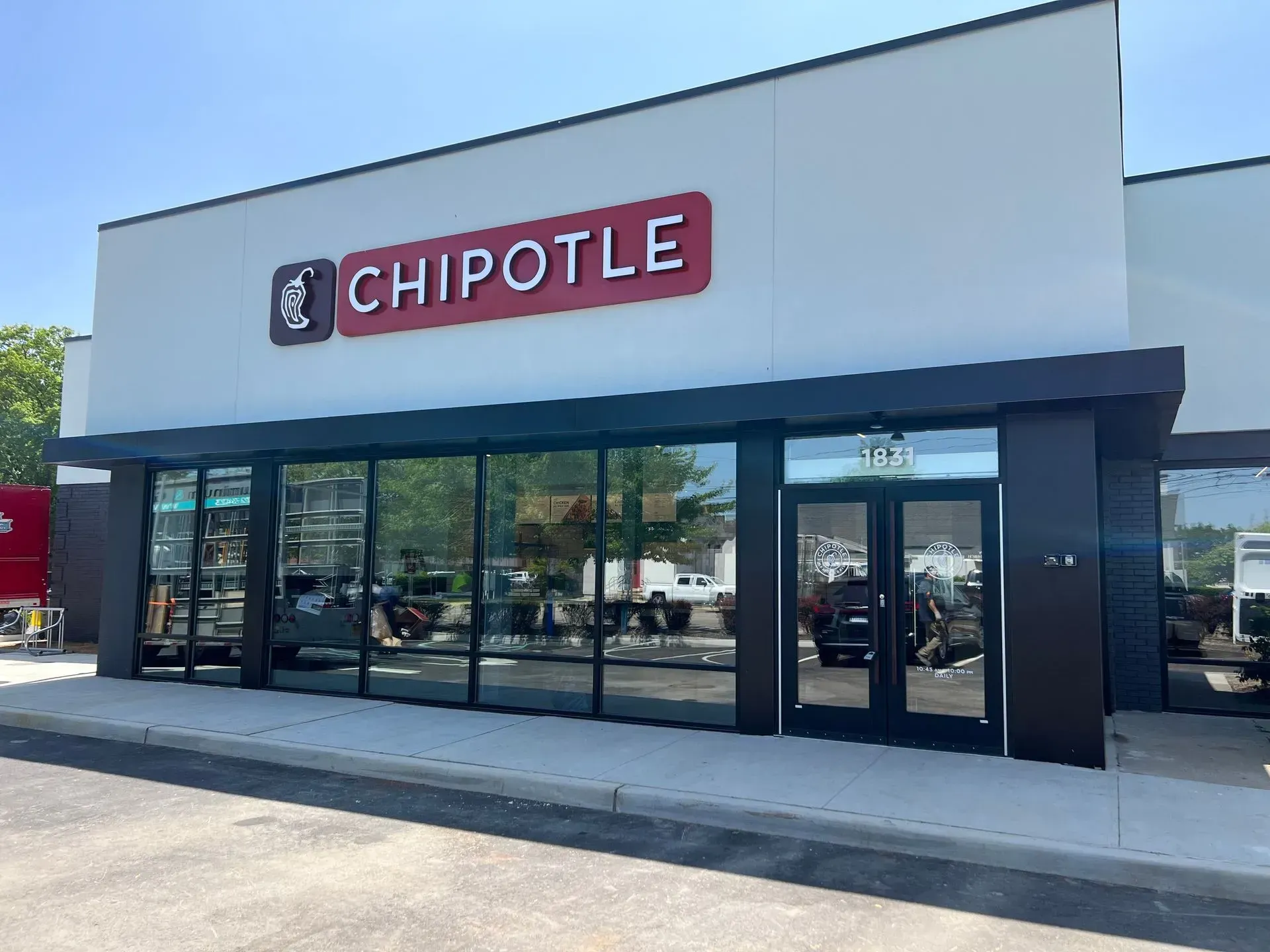 Chipotle restaurant exterior with large windows, red and white sign, and a black awning.