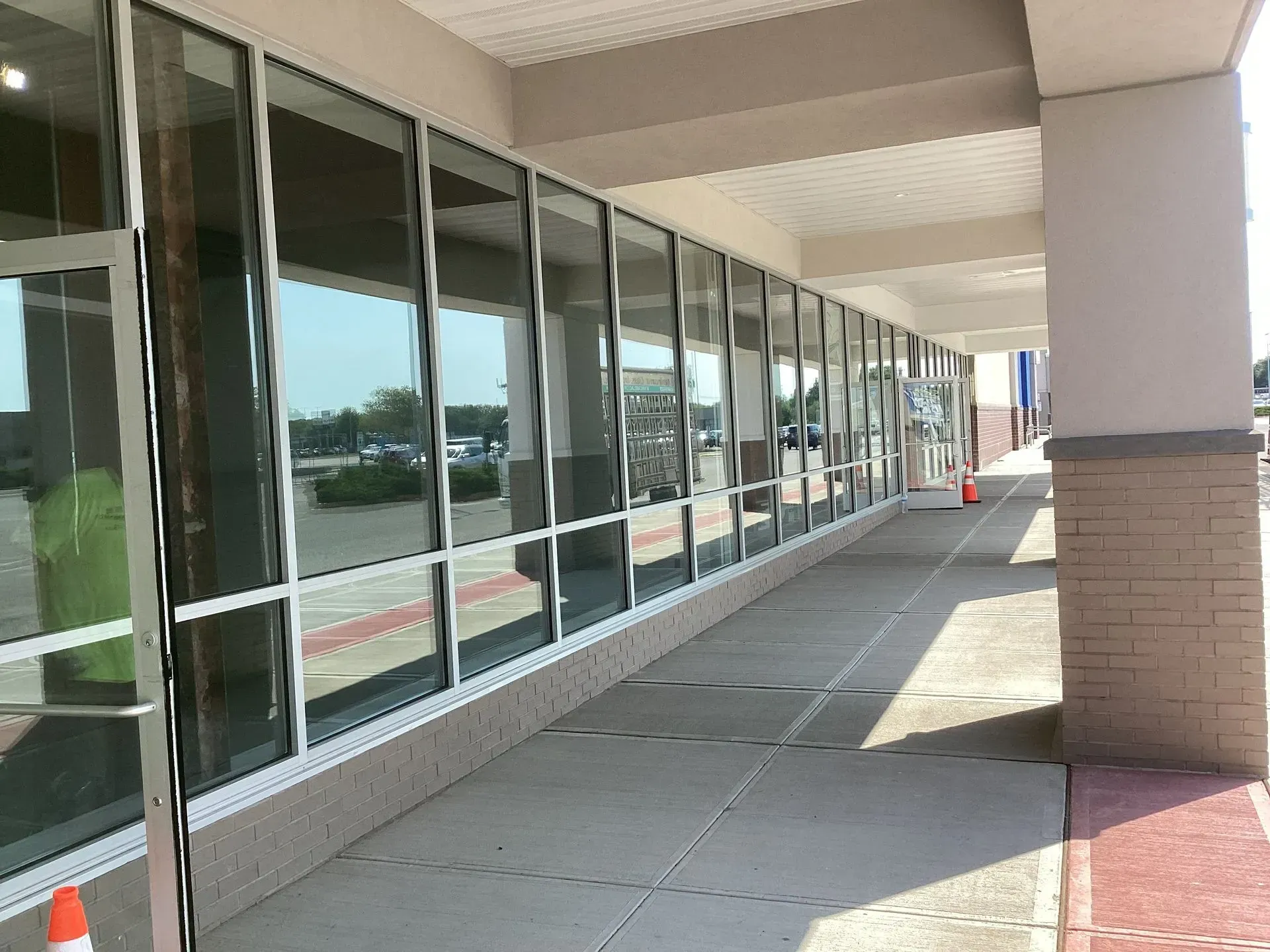Exterior of a building with a long row of windows, sidewalk, and a column in sunlight.