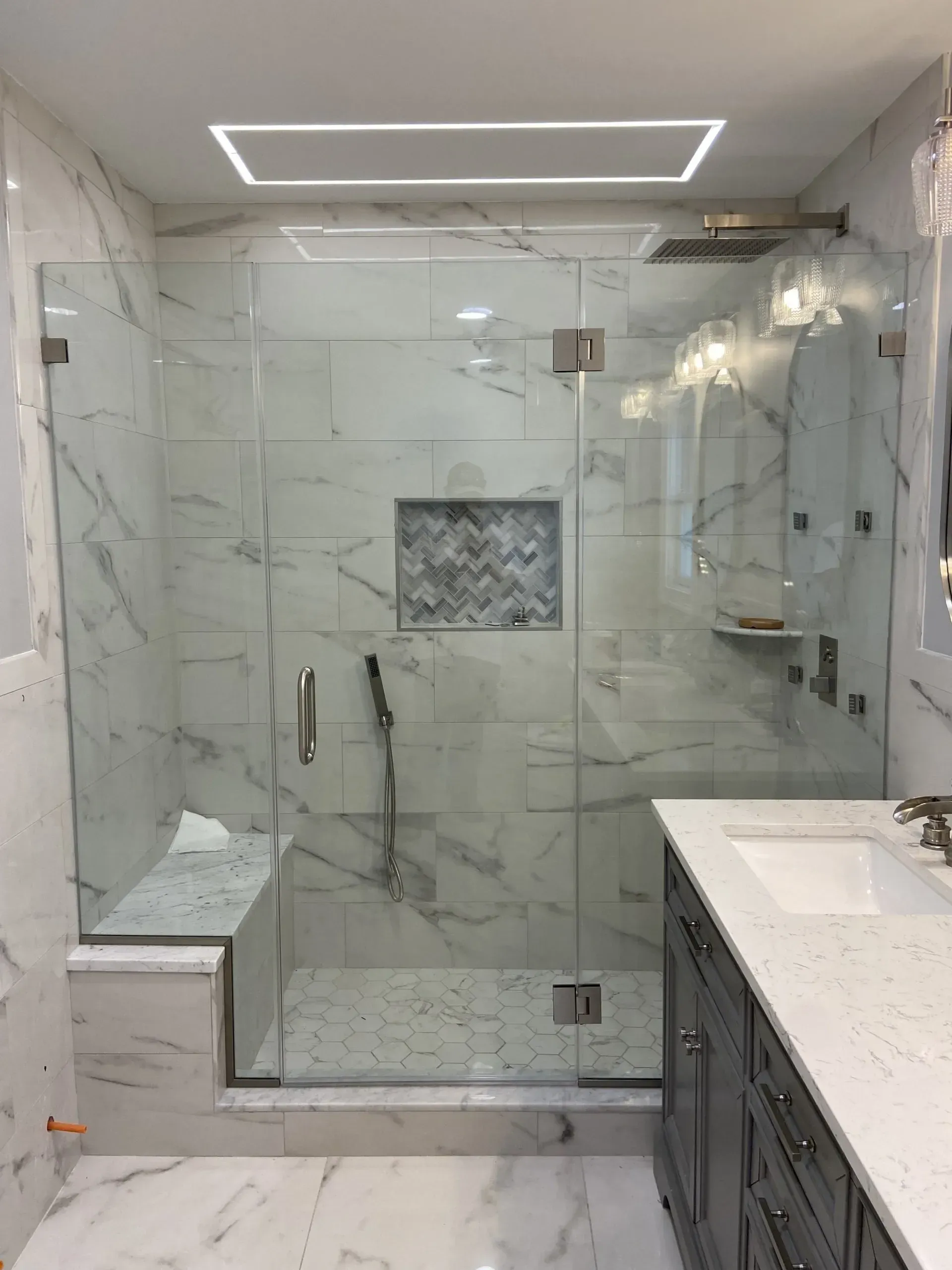 Modern bathroom with a marble-tiled shower, glass door, and vanity with dark cabinets and a white countertop.