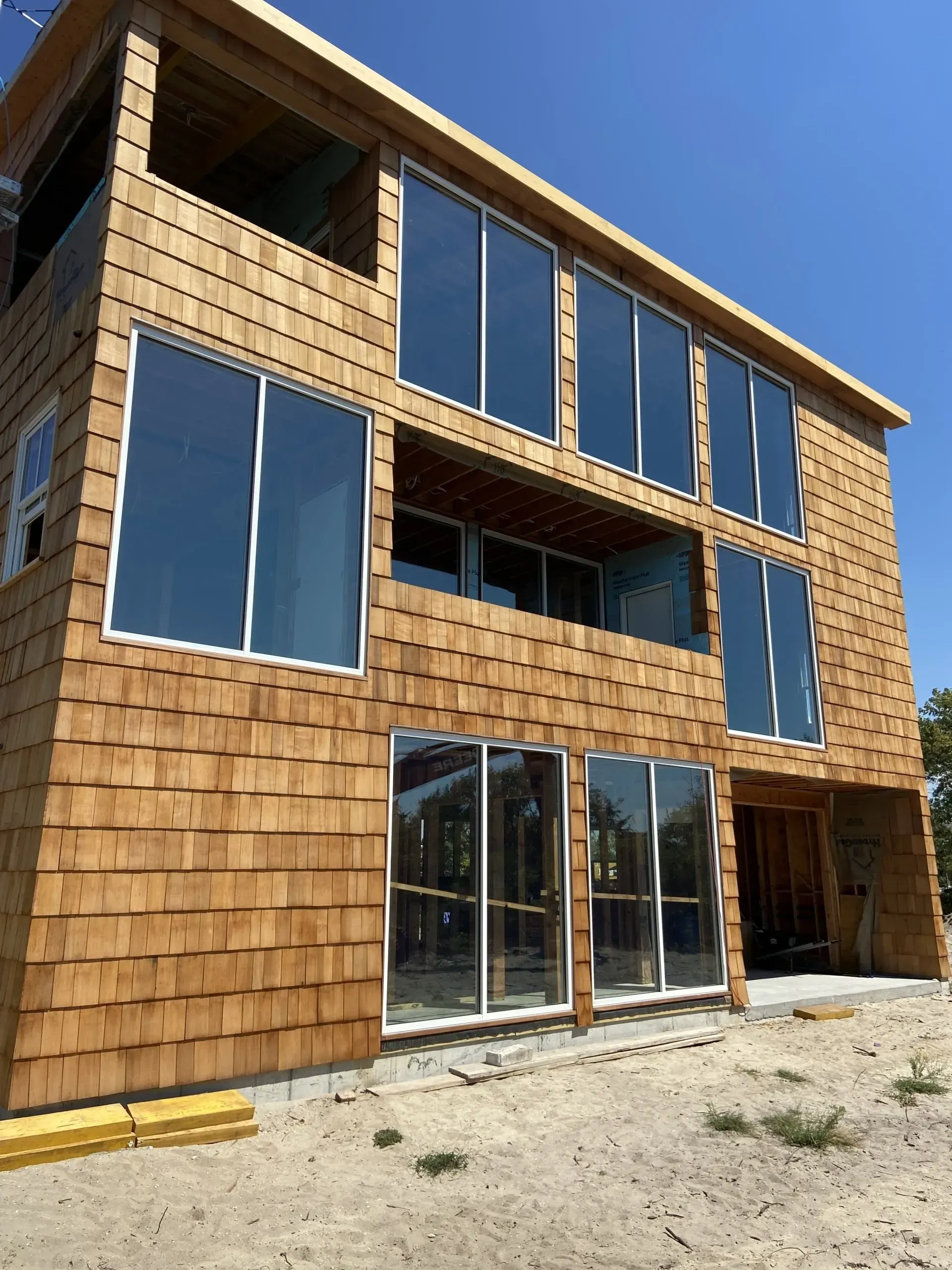 Three-story wood-shingled building with large windows reflecting the sky, under construction.