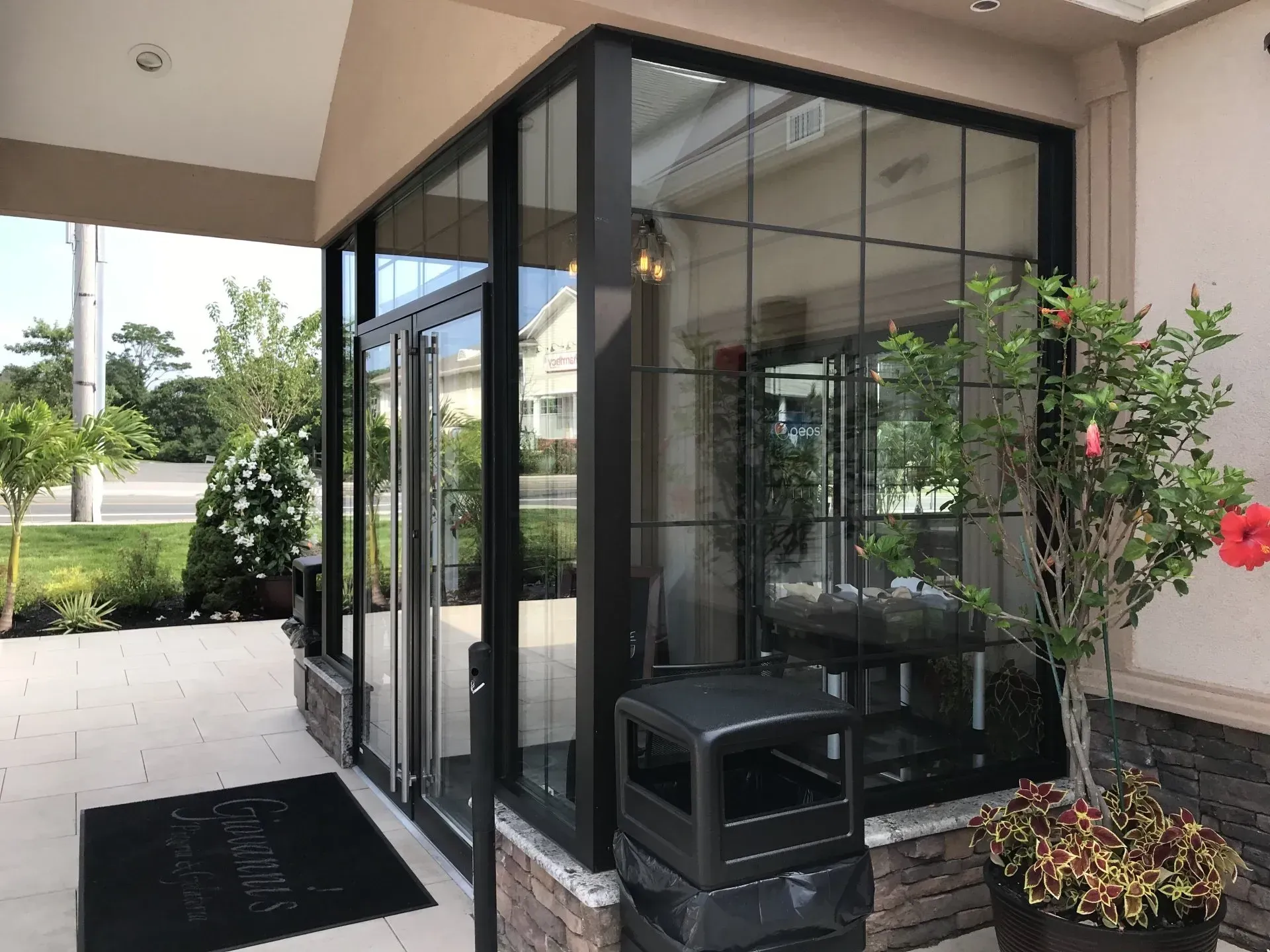 Glass entrance with black trim, potted plants, and a welcome mat.