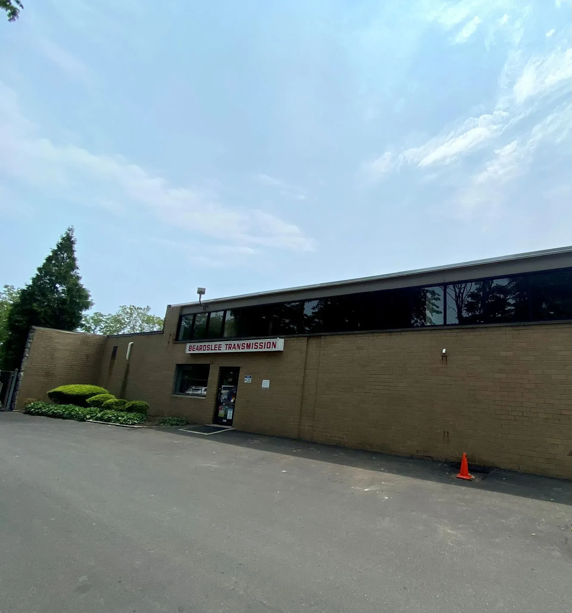 A brick building with large windows under a blue sky, an orange cone sits on the asphalt.