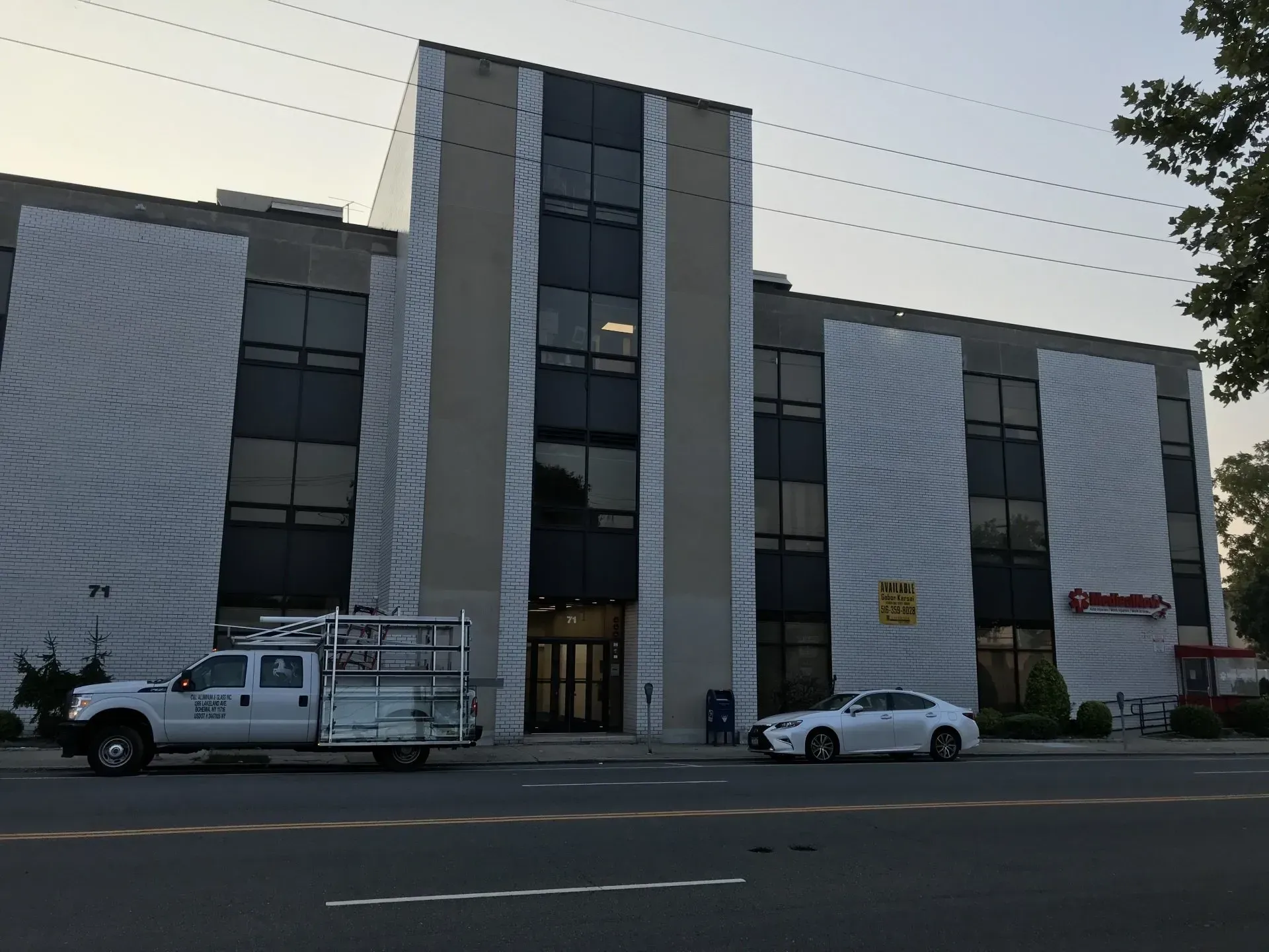 Building exterior with gray facade, windows, and two parked vehicles in front.