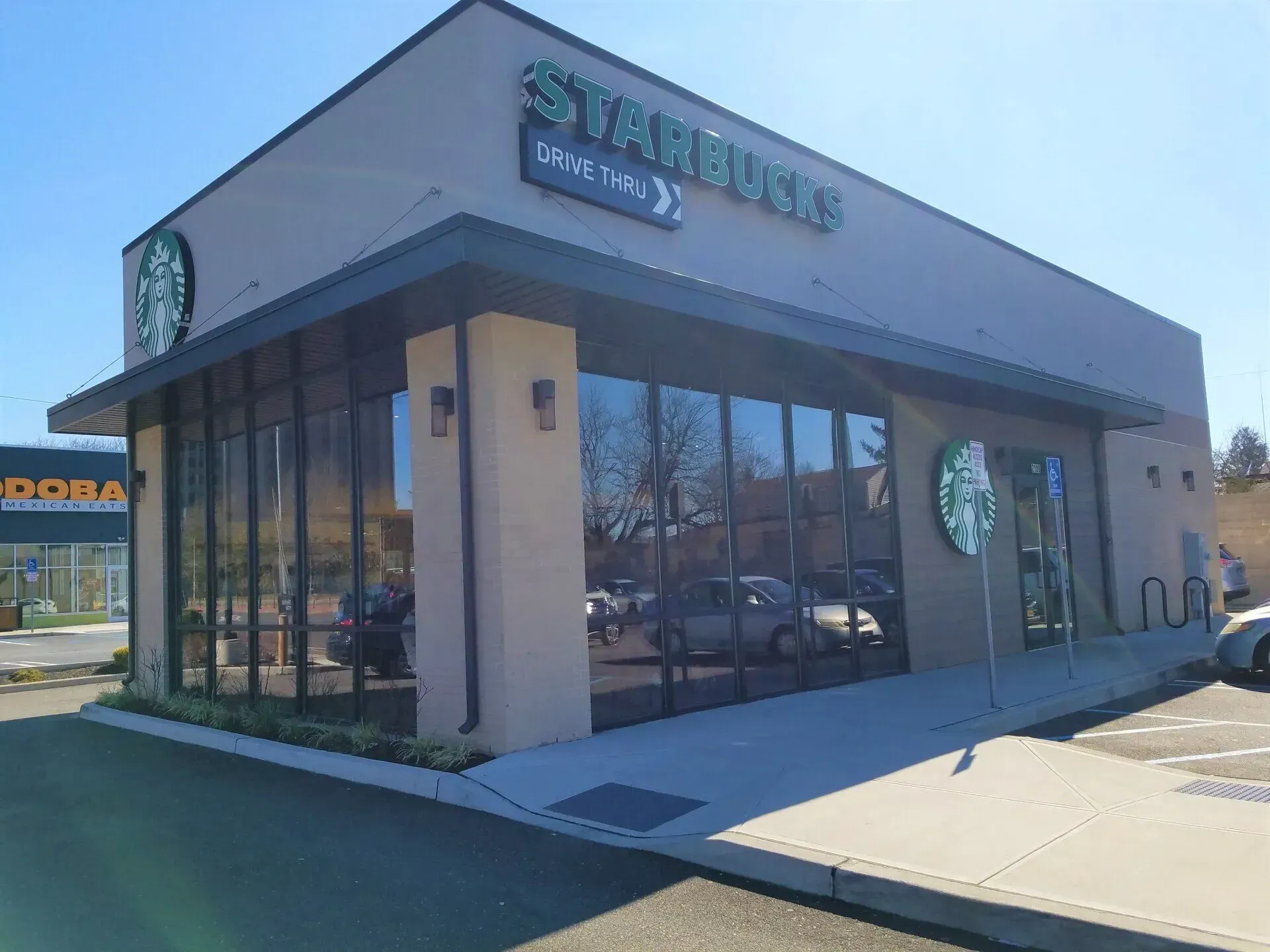 Starbucks building with drive-thru, glass windows, and green logo, on a sunny day.