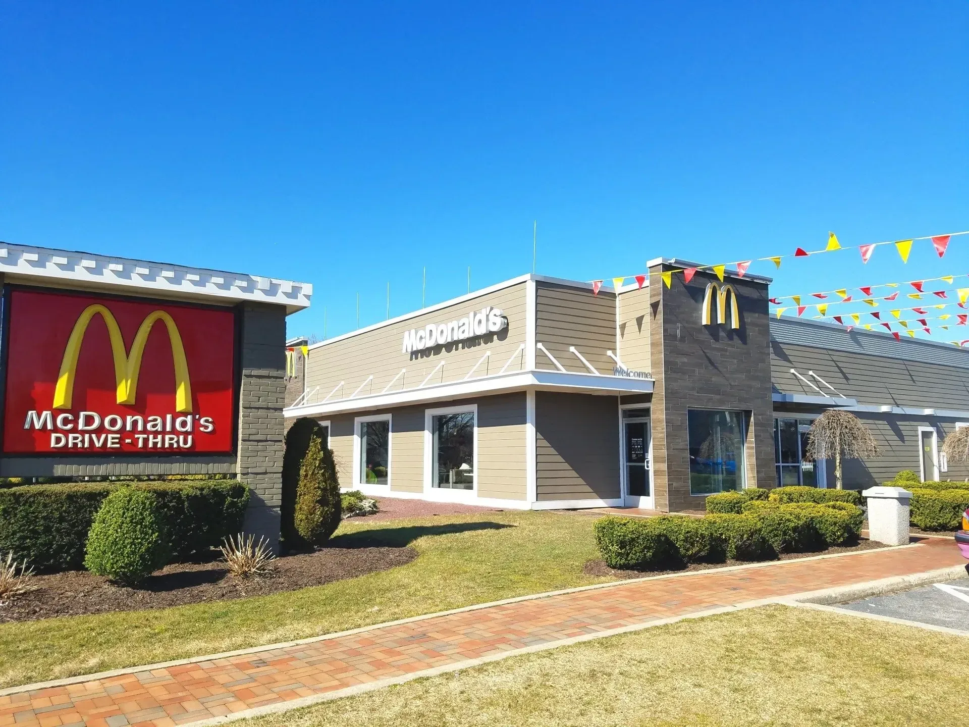 McDonald's restaurant with a red and gold sign, drive-thru, and brown building under a blue sky.