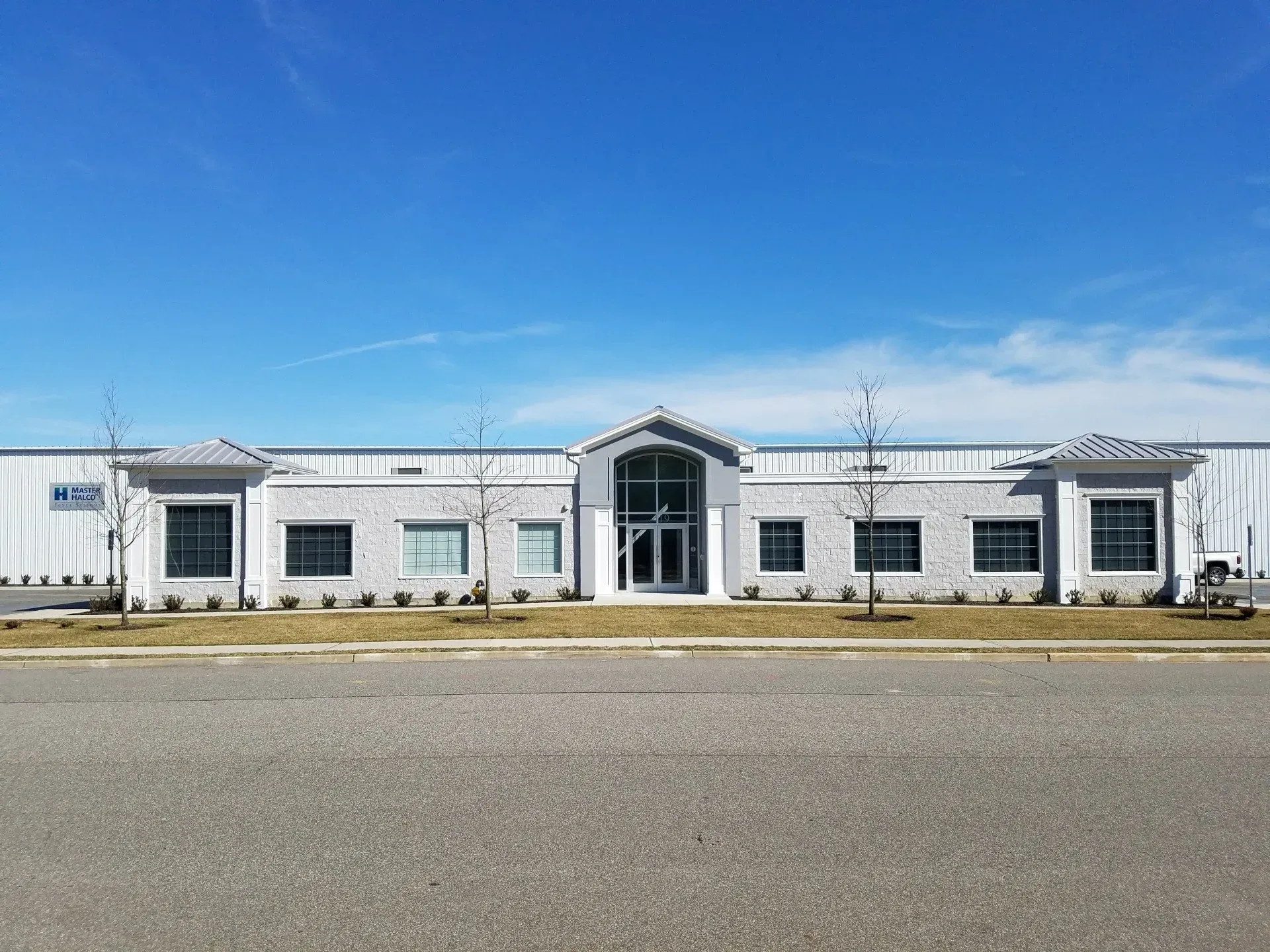 Modern, light-colored brick building with a blue sky. Central glass entrance, symmetrical design, and low bushes in front.